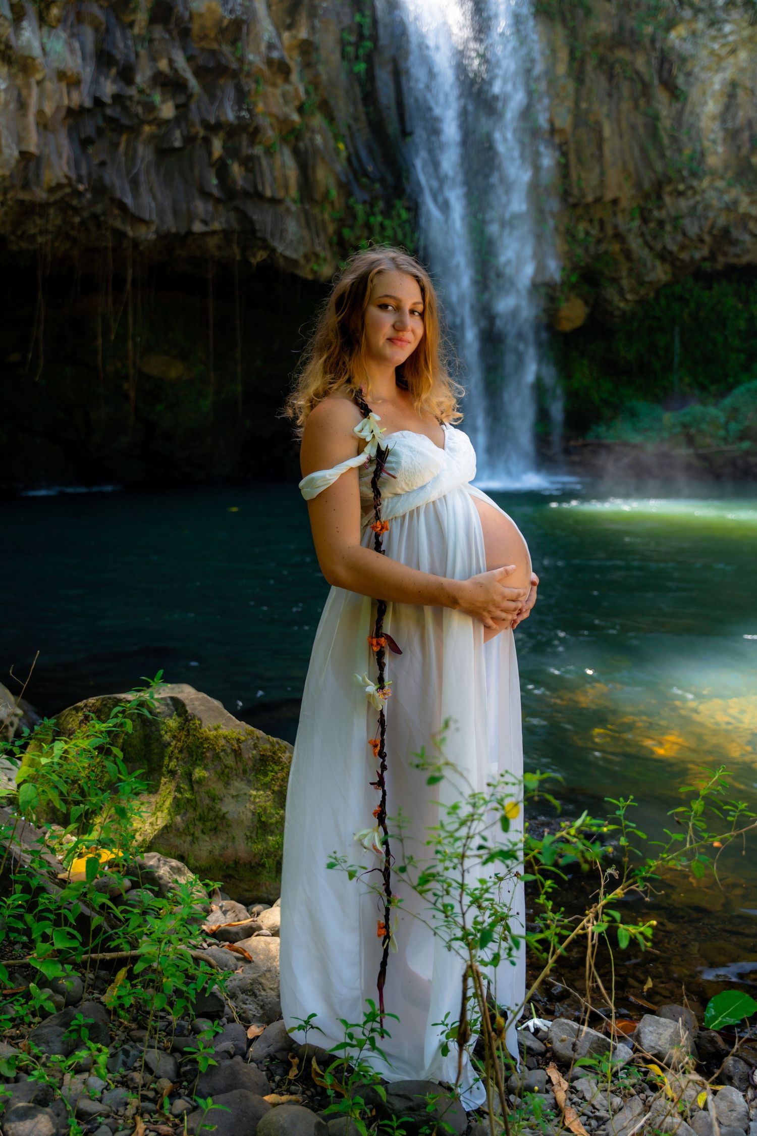 Serene waterfall setting with white dress against lush greenery.