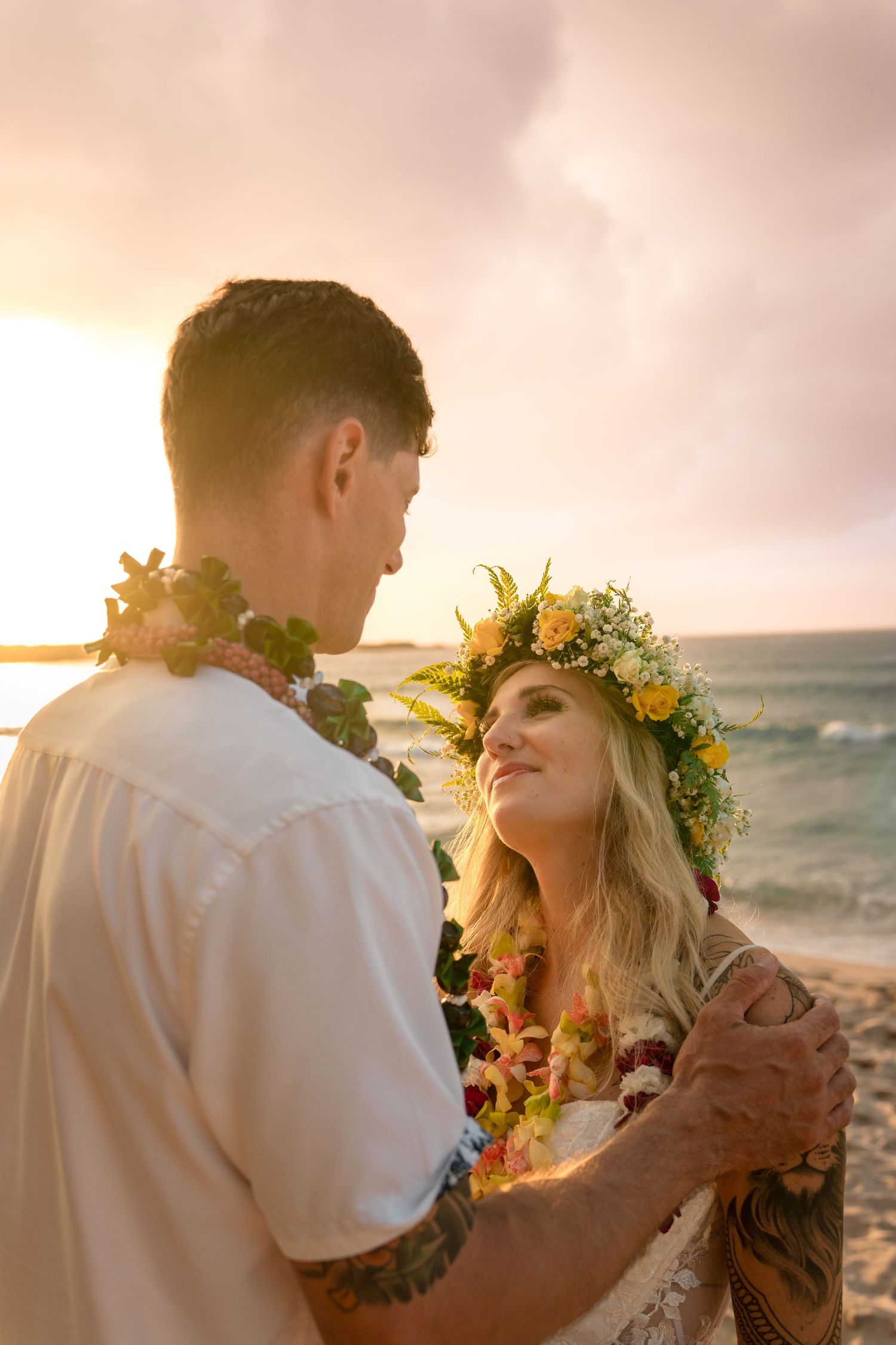 A romantic sunset beach wedding moment with tropical floral decorations.