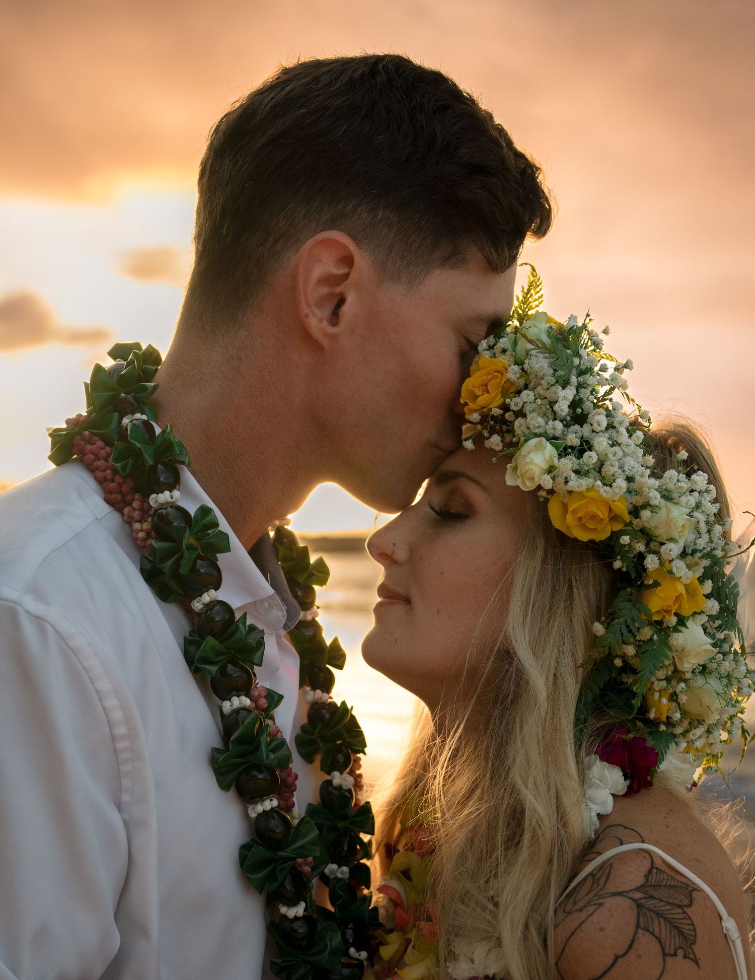 An intimate wedding portrait with flower crowns and leis during golden hour.
