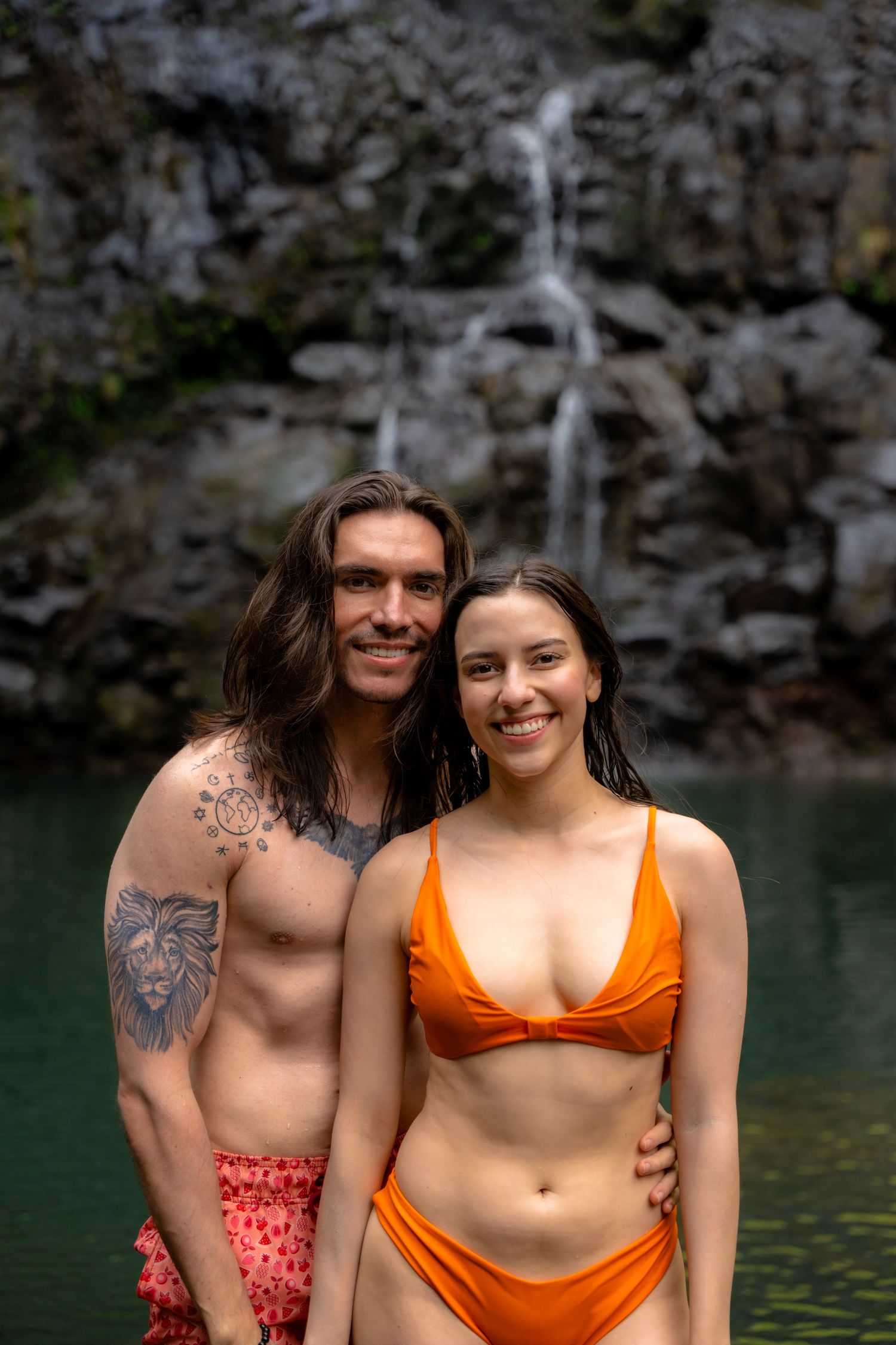 Two swimmers enjoy the refreshing waters beneath a tropical waterfall in Hawaii.
