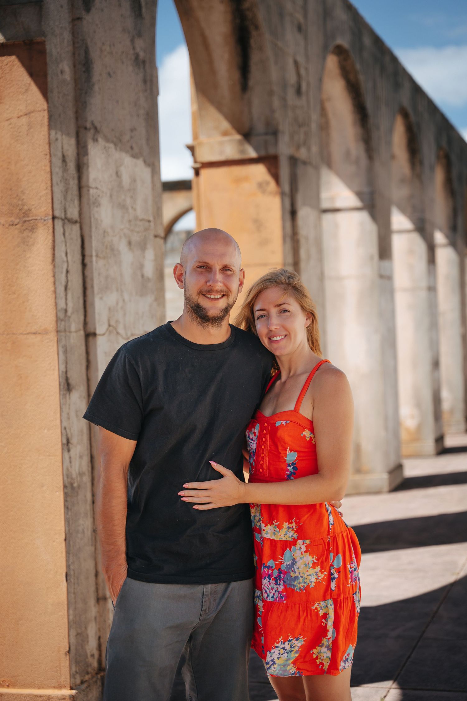 Couple posing together under concrete archway structure in warm sunlight.