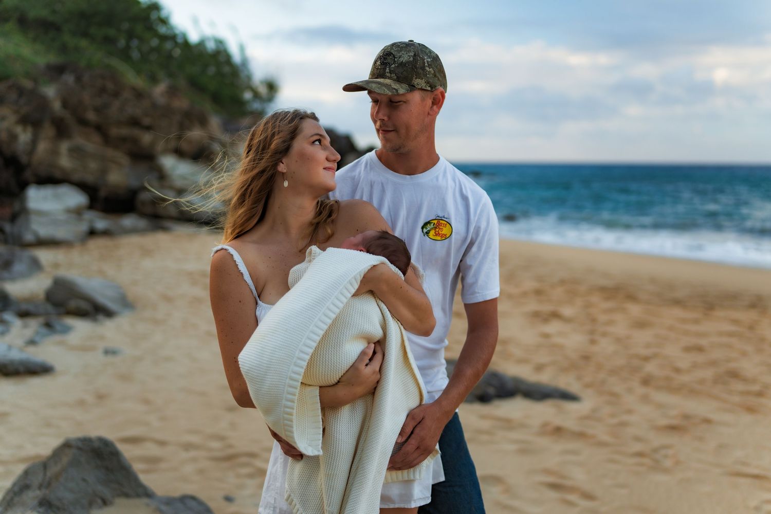 Romantic couple withe a newborn embracing on a tropical beach at sunset with waves crashing in the distance.