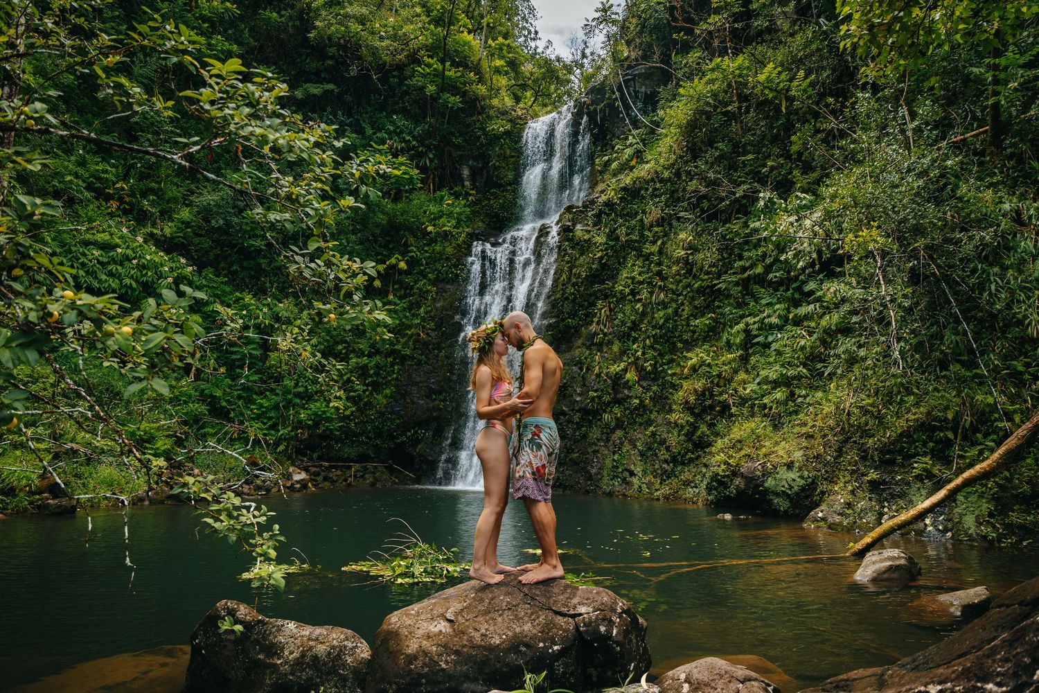 Couple sharing romantic moment by waterfall in tropical forest setting.
