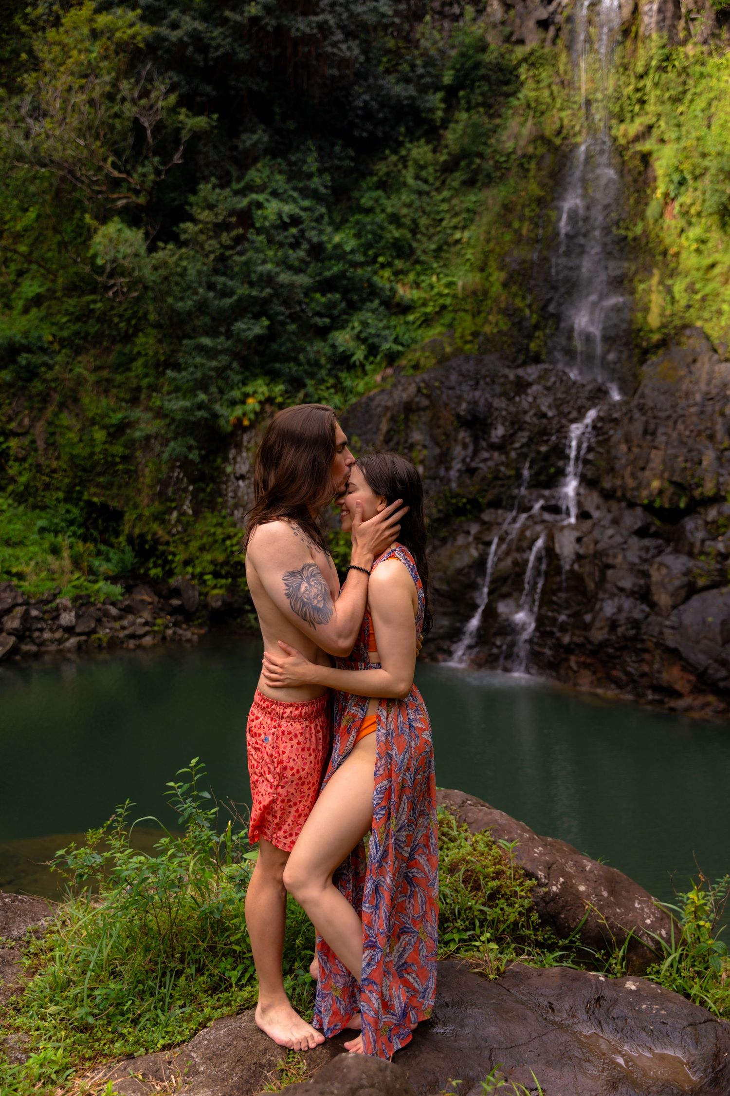 A romantic moment captured in front of a cascading waterfall with a turquoise pool below.