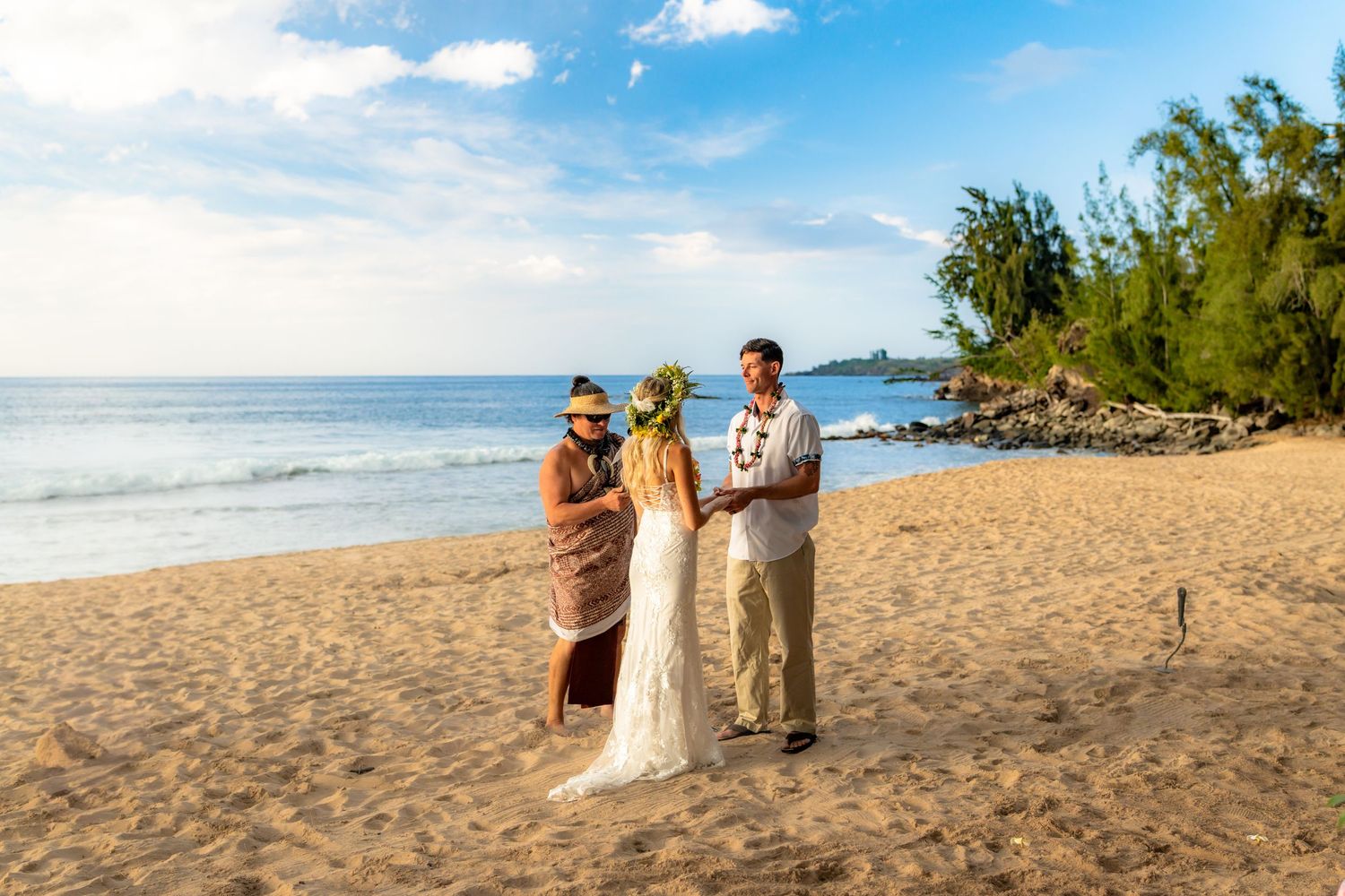 A beachside wedding ceremony unfolds under blue skies with palm trees in the background.
