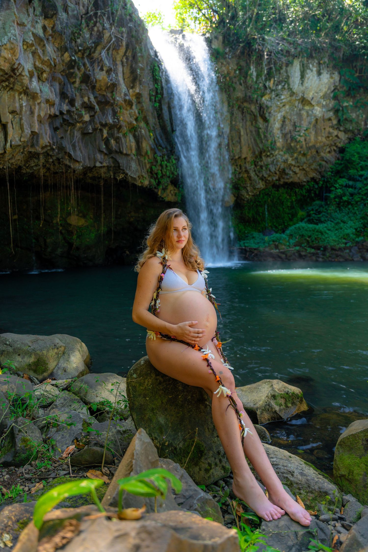 Person in white dress sitting on rocks by a cascading waterfall.