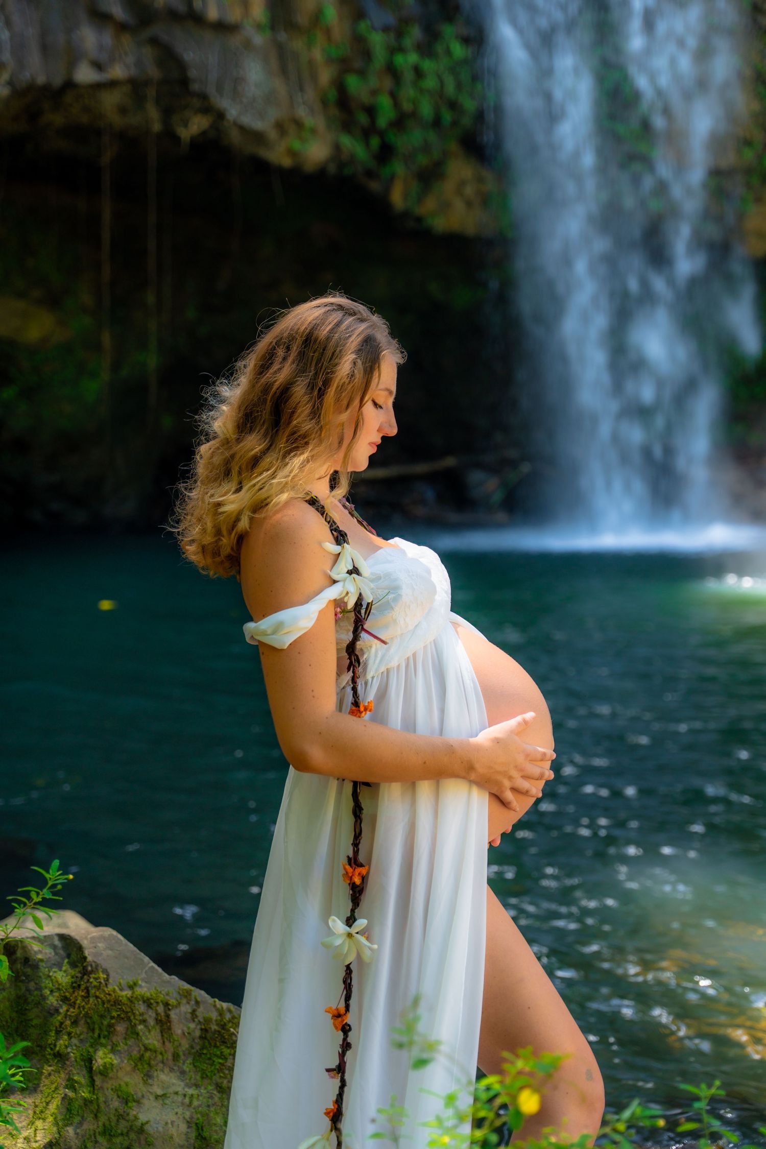 Flowing white dress contrasts against dramatic waterfall backdrop.