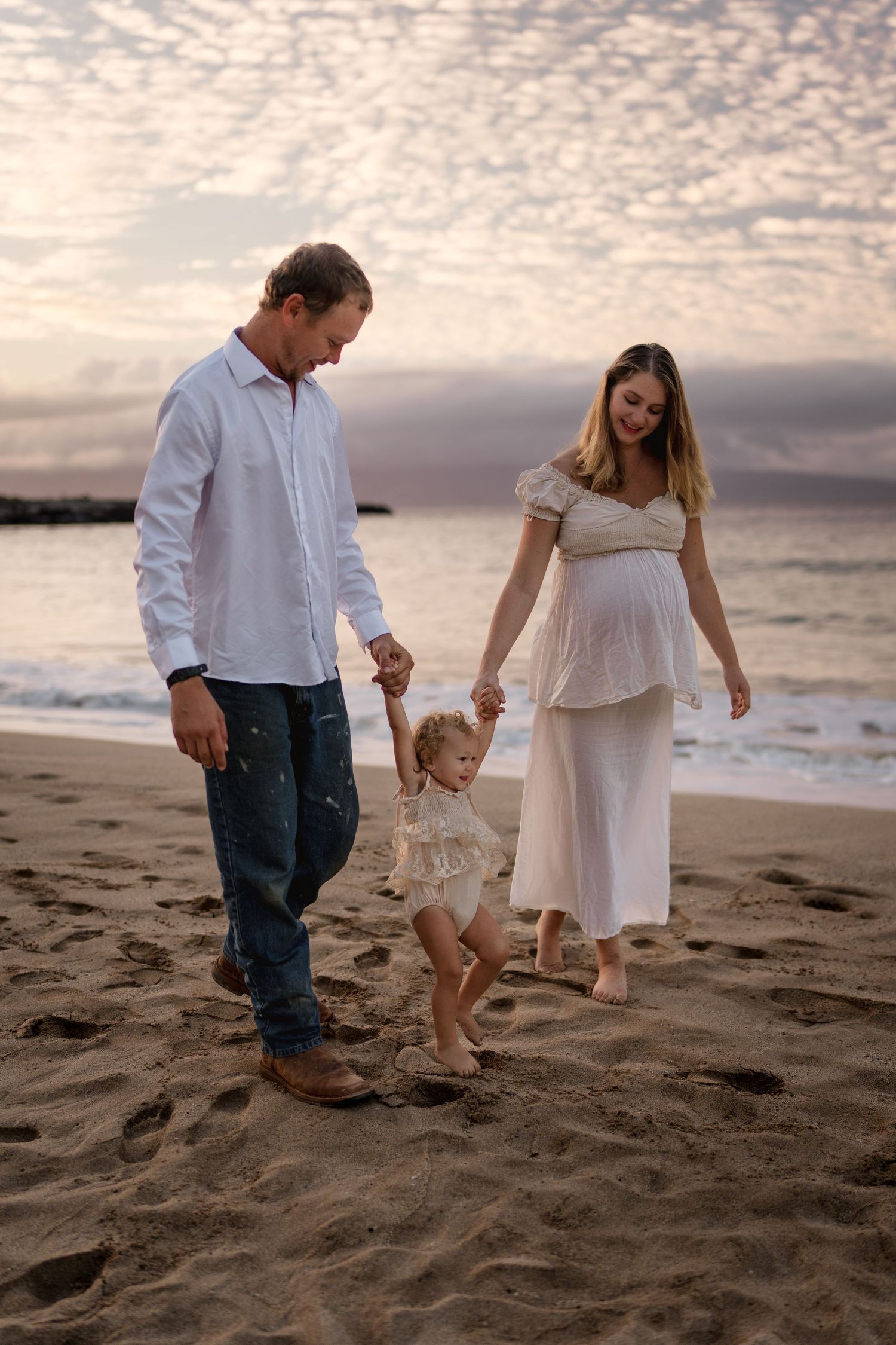 Family walking together on sandy beach at sunset in coordinated white outfits.