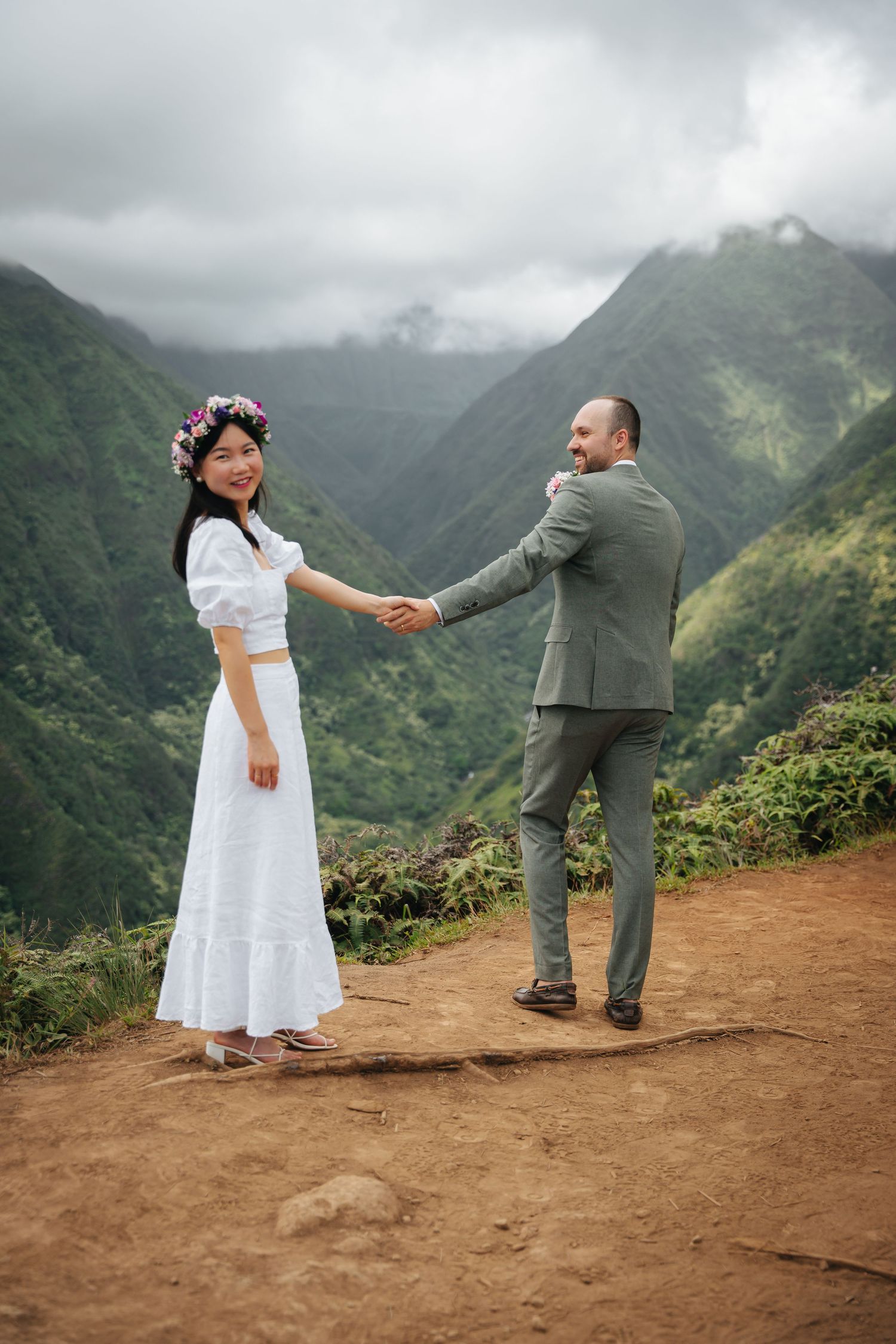 A couple dances playfully on a dirt path overlooking misty mountain valleys.