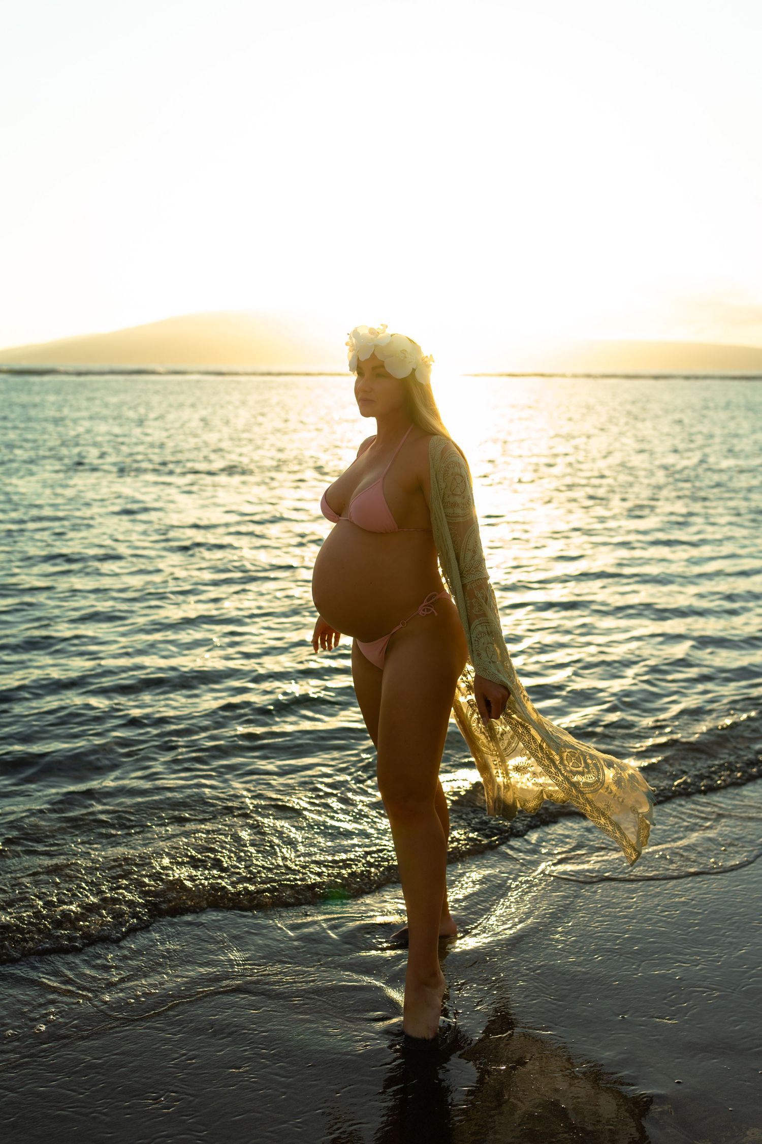 Silhouette of pregnant woman walking in ocean waves during golden hour.
