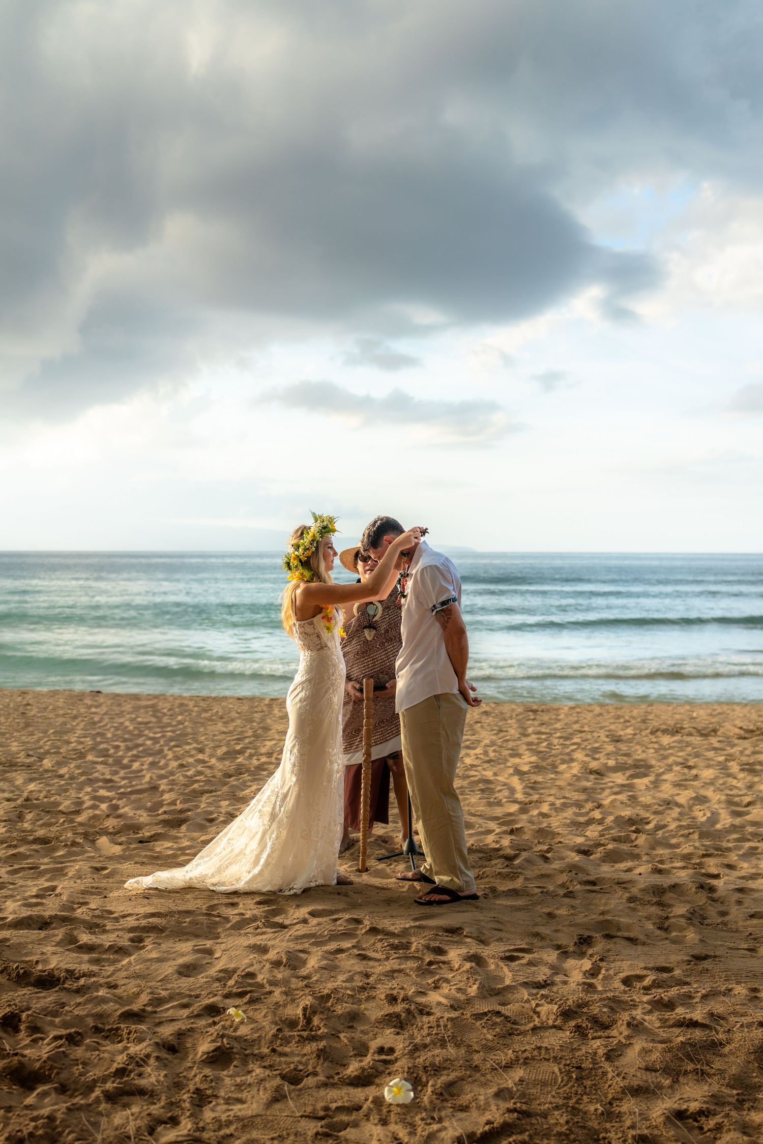 A beach wedding ceremony takes place at sunset with a couple and officiant on the sandy shore.