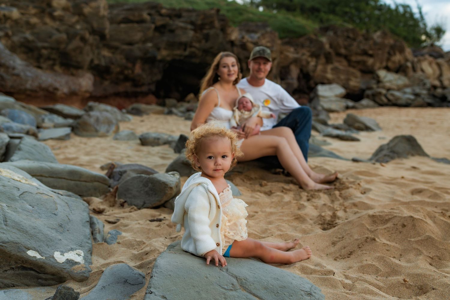 Family enjoying a sunny day at a beach with volcanic rocks and sand.