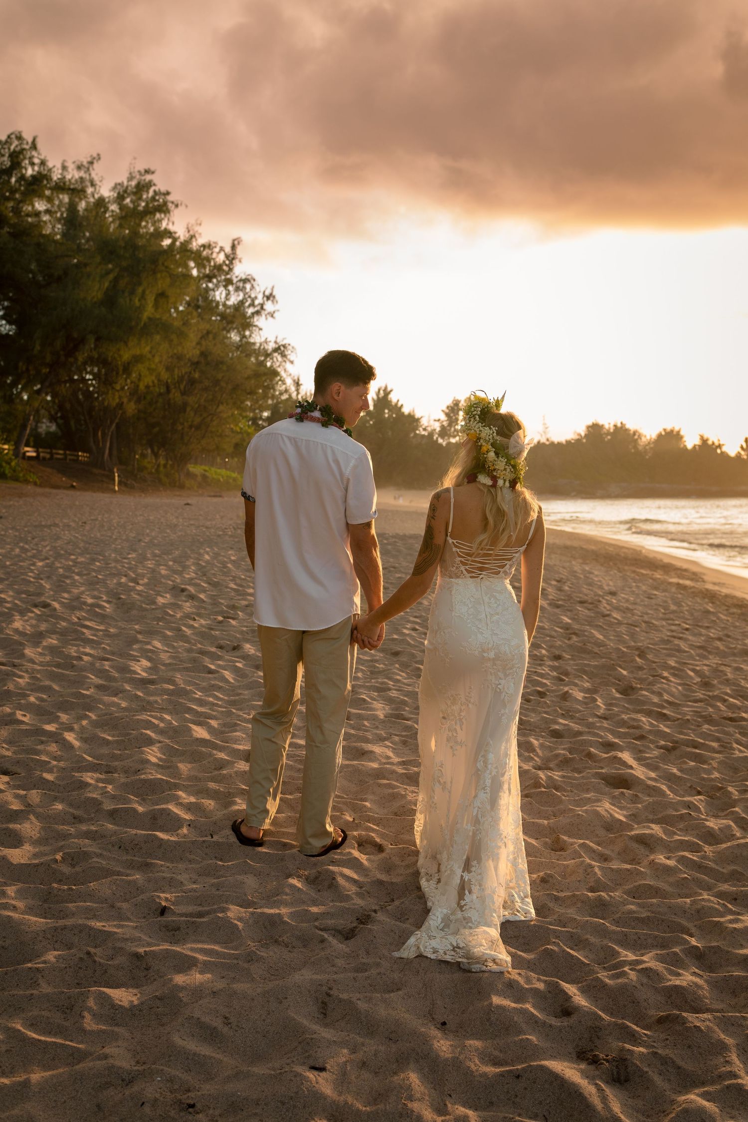 A couple walks hand in hand on a beach at sunset after their wedding ceremony.