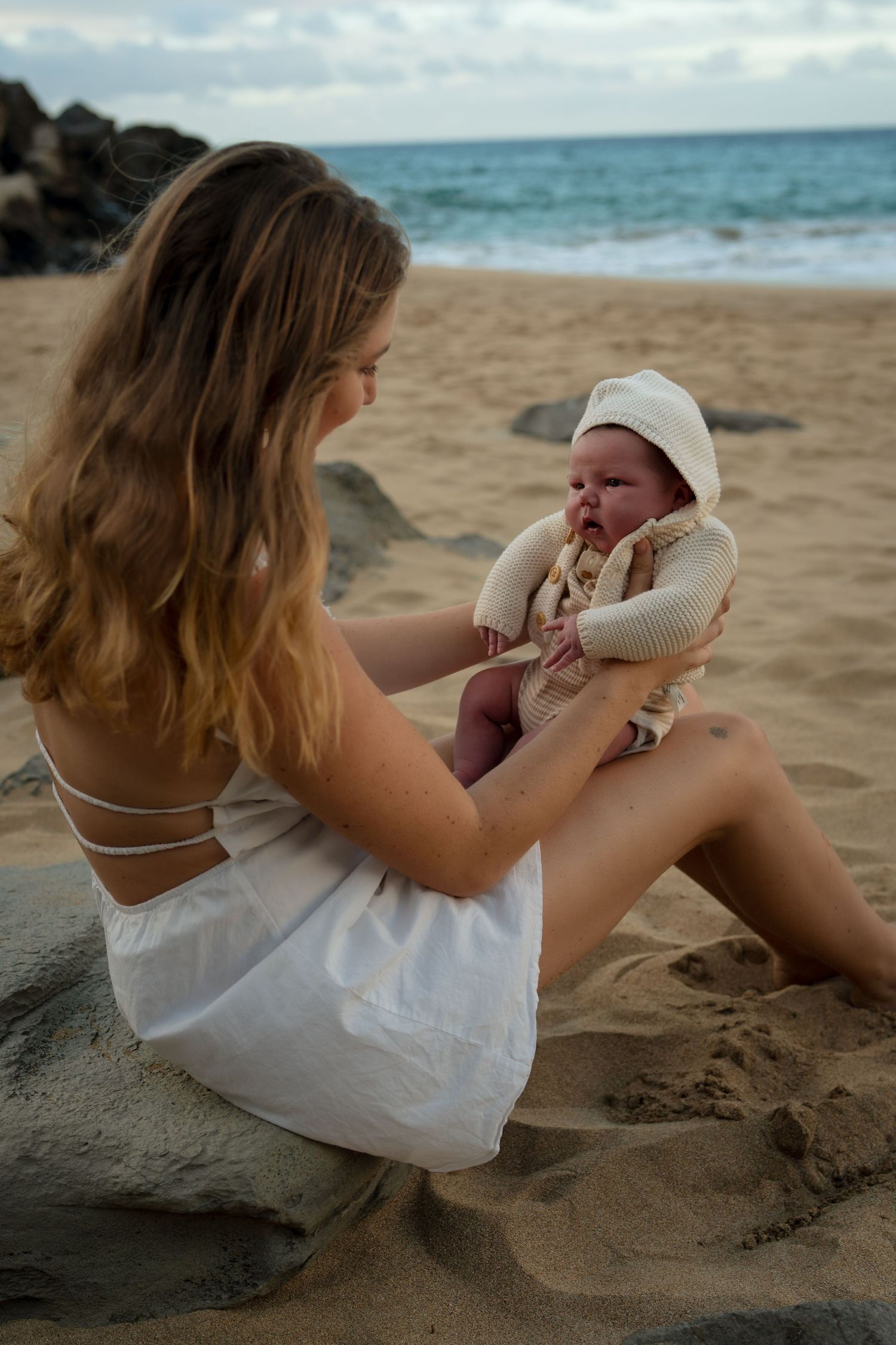 Mother and baby share tender moment on sandy beach at sunset.