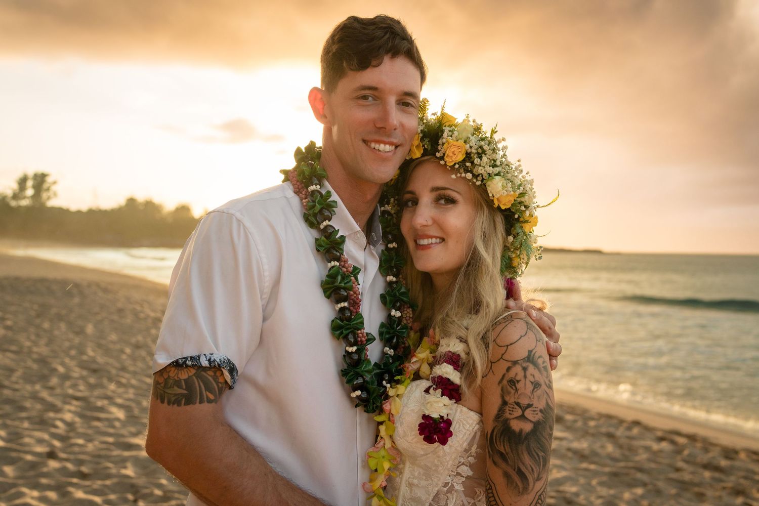 A beach wedding couple wearing traditional Hawaiian leis poses at golden hour.