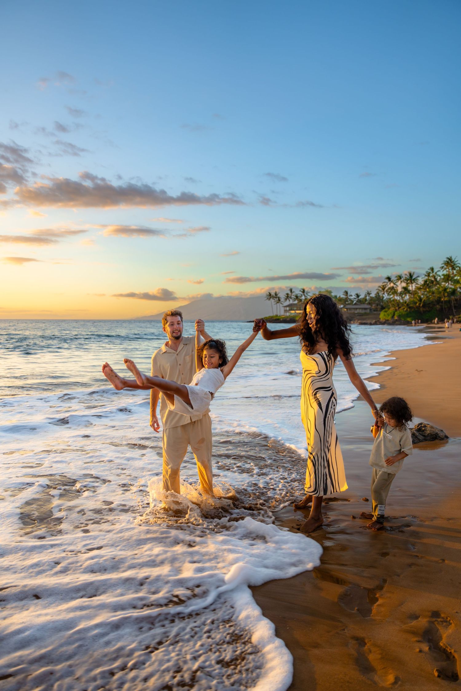 Family playing and jumping in ocean waves at sunset on a tropical beach.