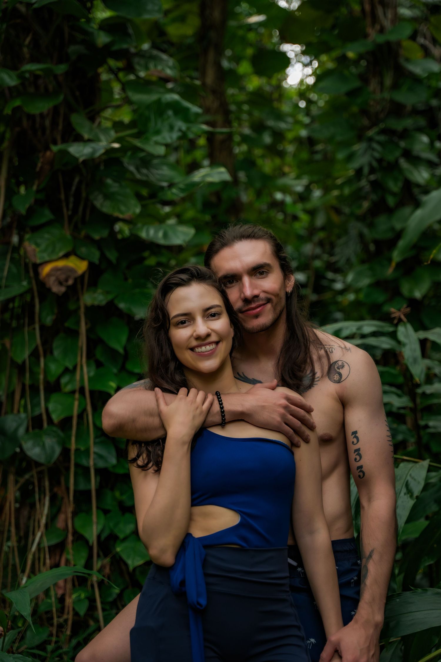A couple embraces in a lush garden setting wearing blue attire against green foliage.