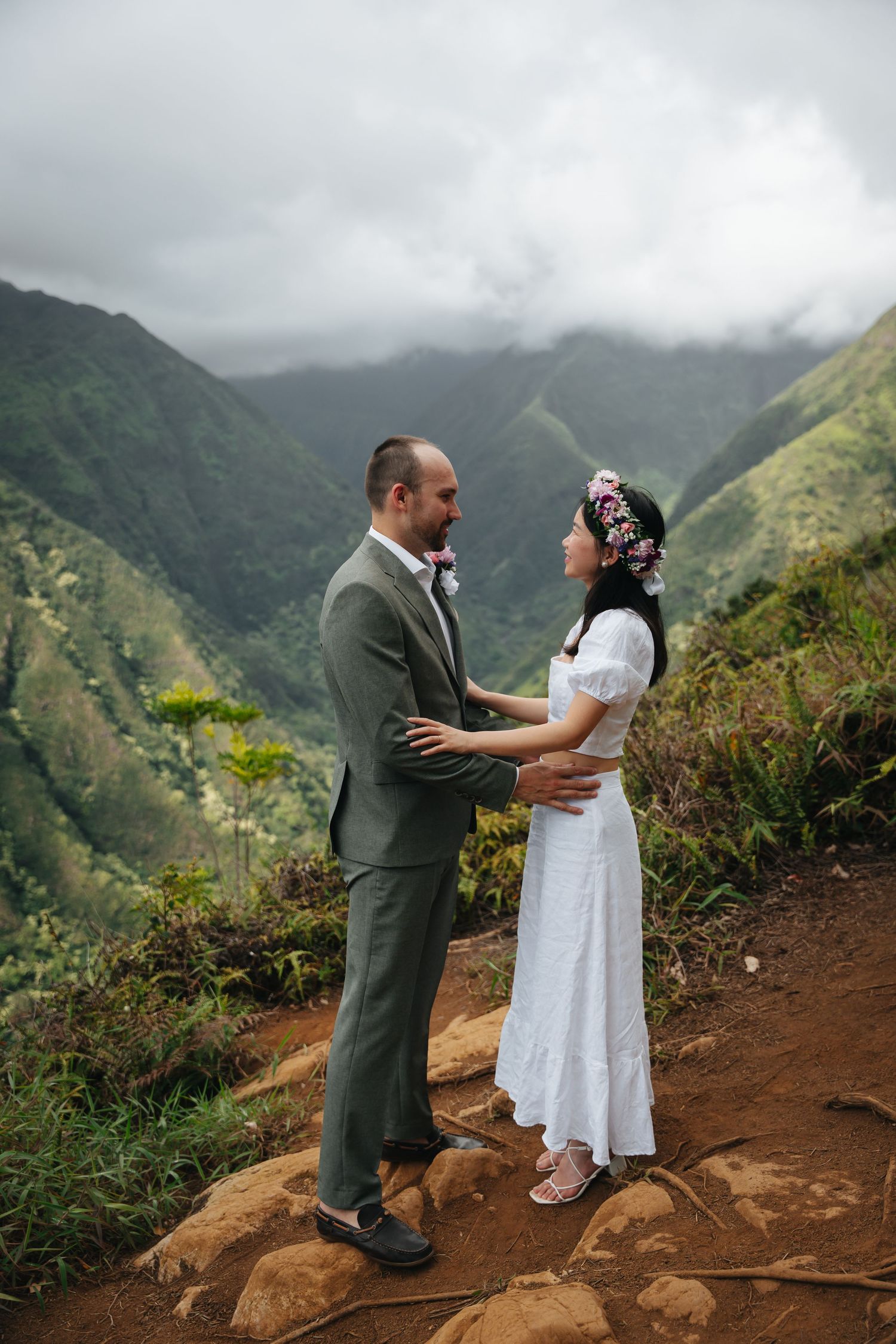 Intimate moment between couple on mountain trail with misty valley backdrop.