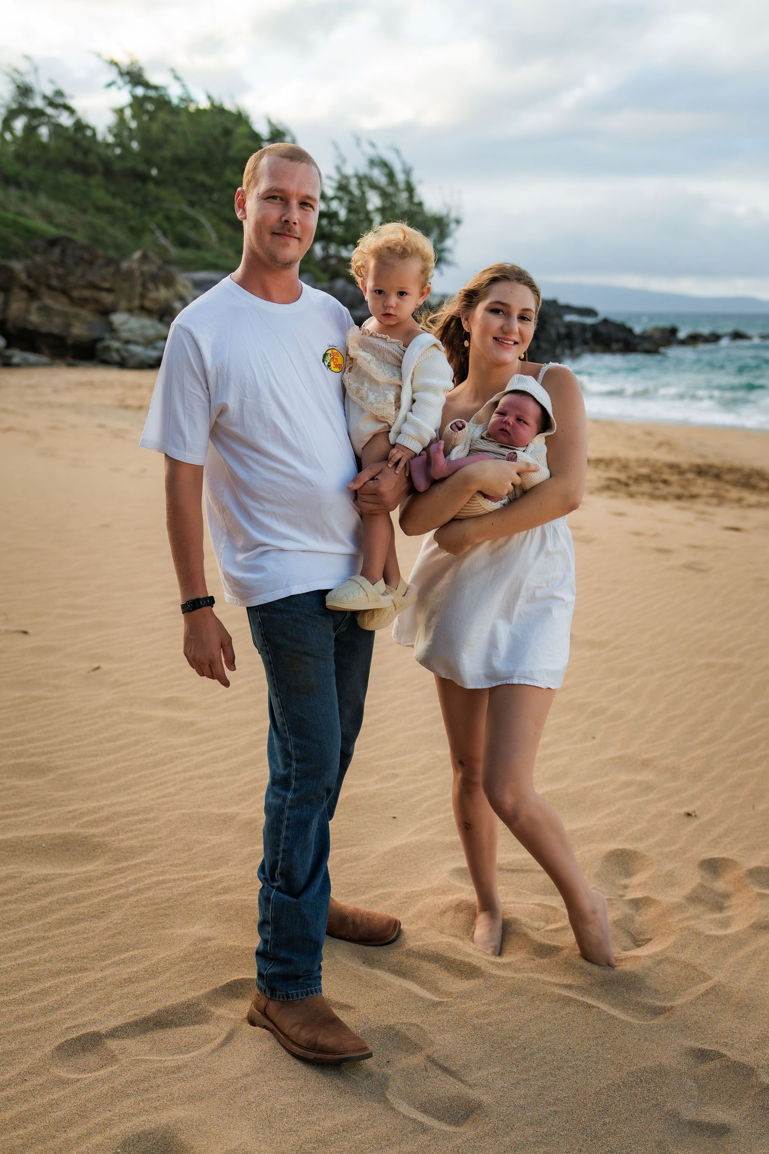 A family plays together on a sandy beach with ocean waves and rocky cliffs in the background.