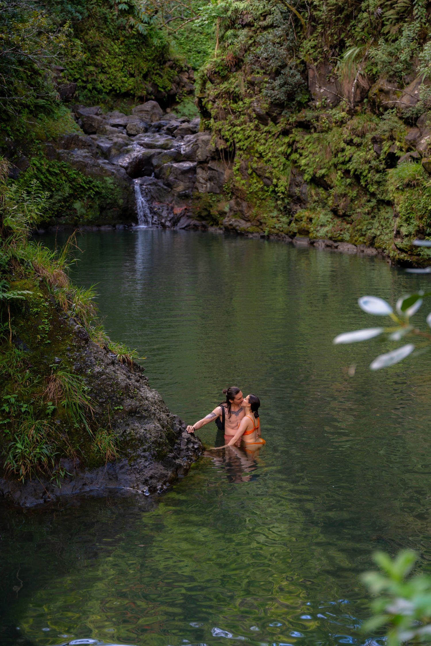 Two swimmers enjoy the emerald waters of a secluded tropical waterfall pool.