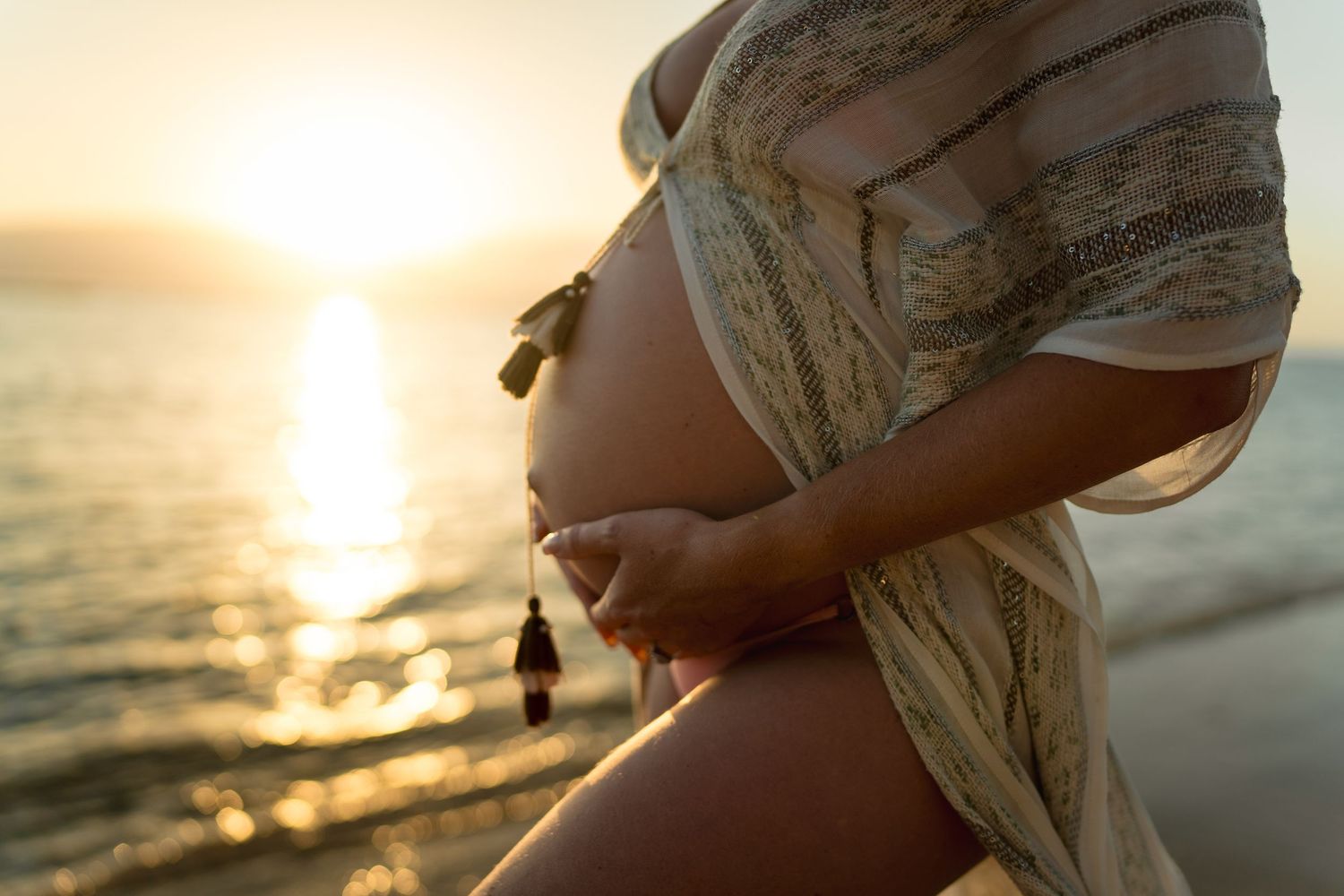Maternity beach photography with flowing fabric against setting sun.
