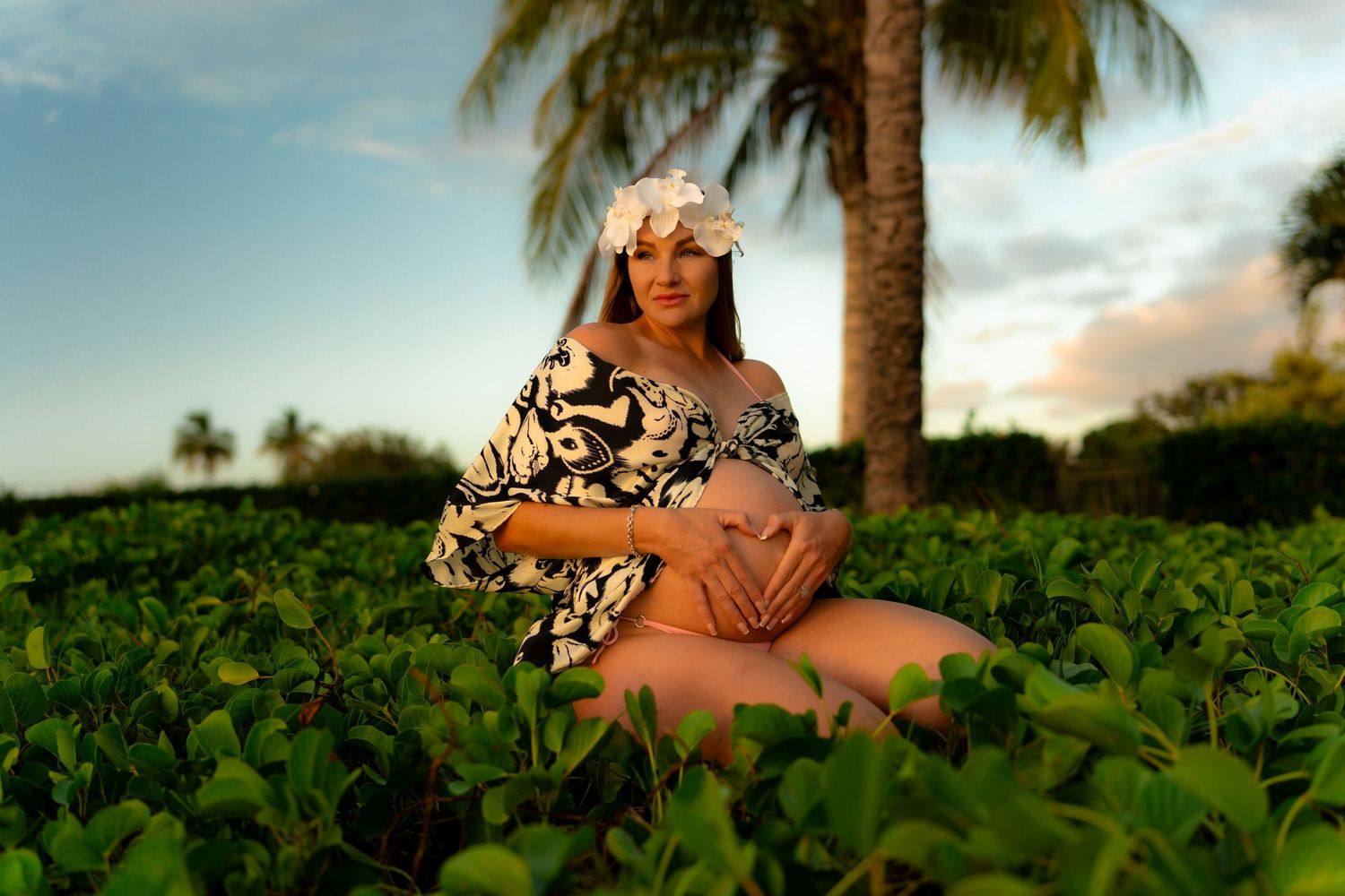 Tropical maternity photoshoot among lush palm trees and greenery.