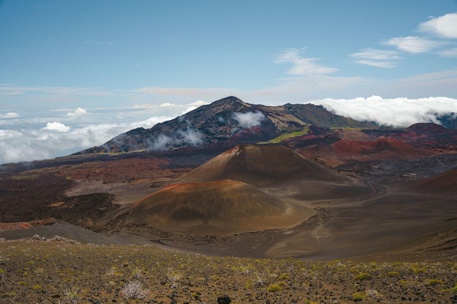 Panoramic view of Haleakala's volcanic crater landscape with clouds rolling over mountains.