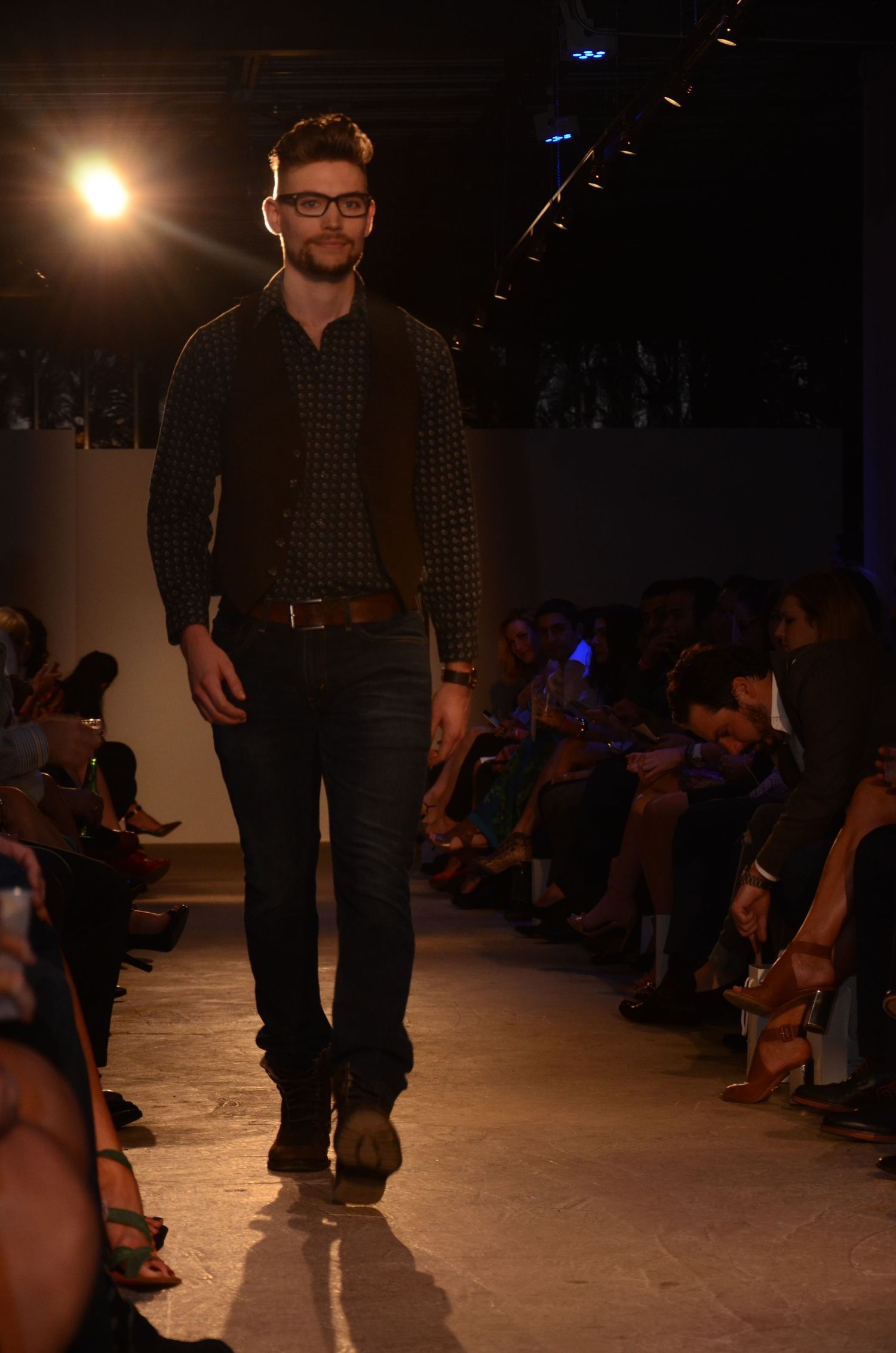 Fashion model showcases casual menswear with plaid shirt and dark jeans on runway.