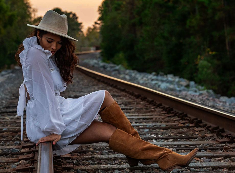 Fashion portrait on railroad tracks featuring white dress and brown cowboy boots.