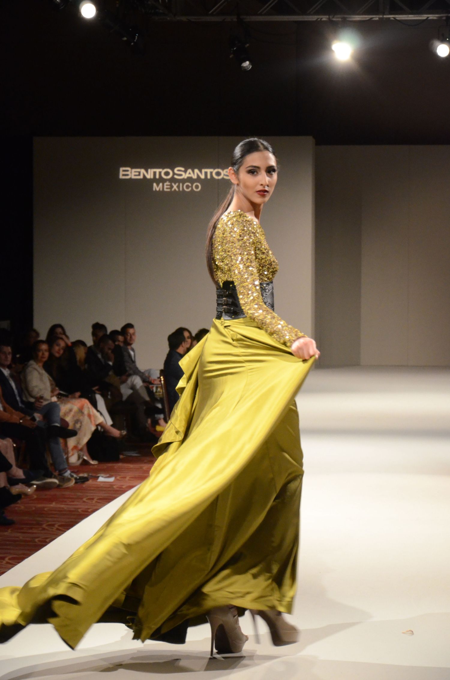 A fashion model walks the runway in a dramatic yellow evening gown with long sleeves.