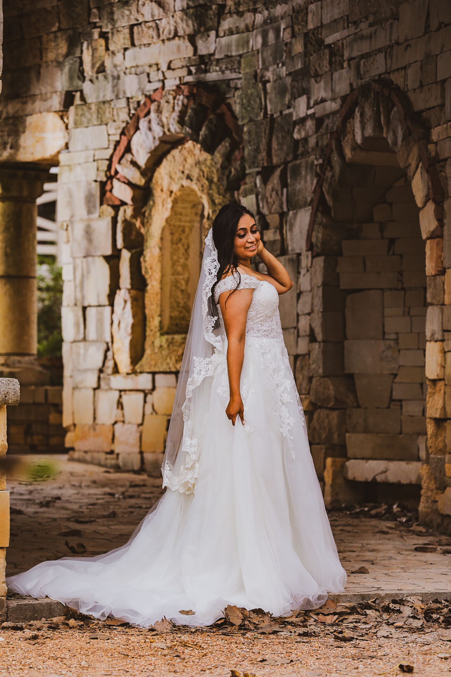 An elegant bridal portrait showcasing a lace wedding dress against weathered stone archways.