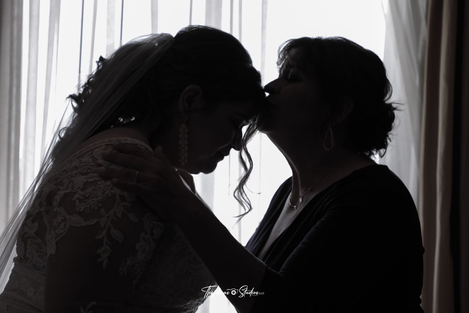 A silhouetted tender moment between two people against a backlit window with sheer curtains.