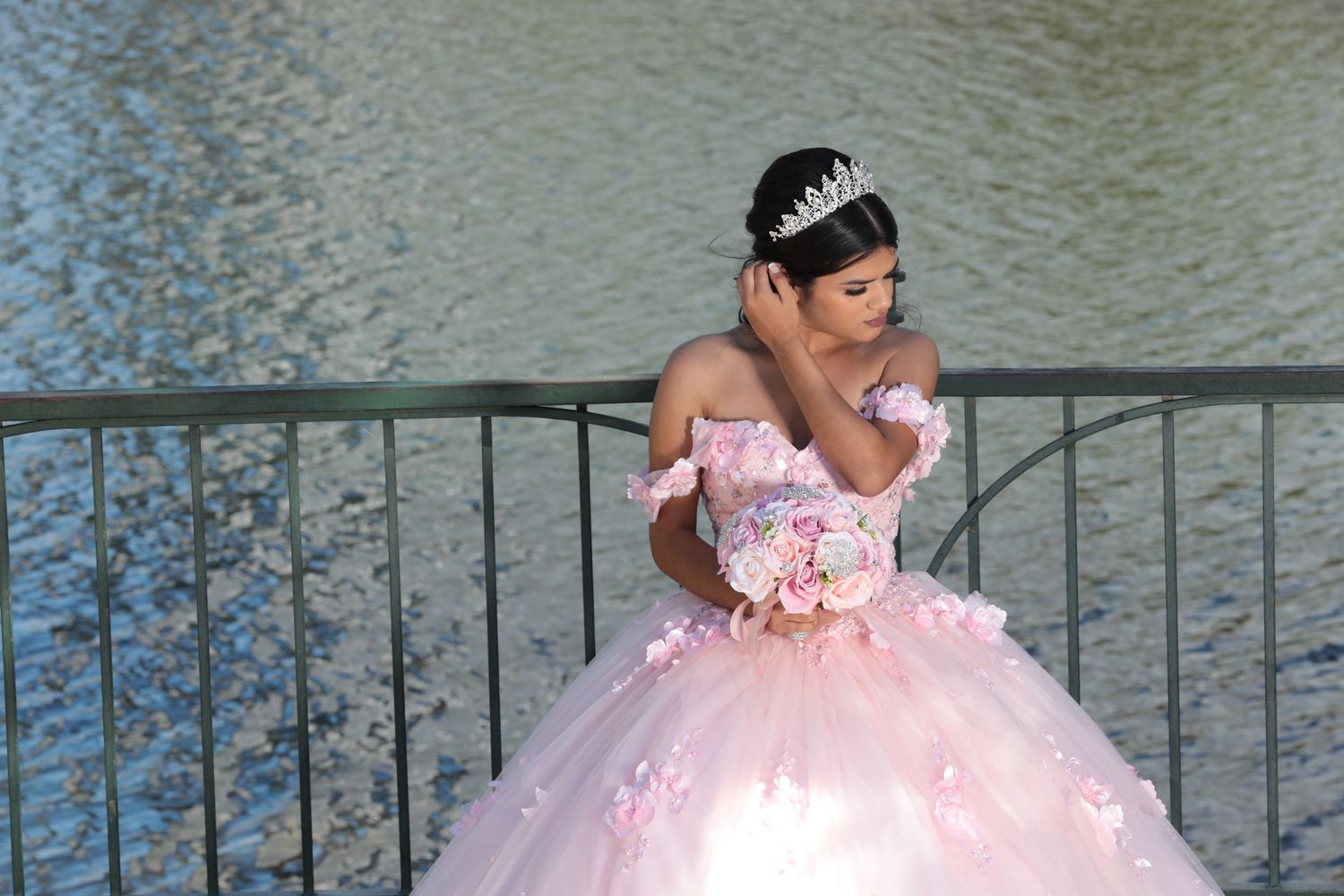 A person in a pink ball gown poses by a railing holding a bouquet.