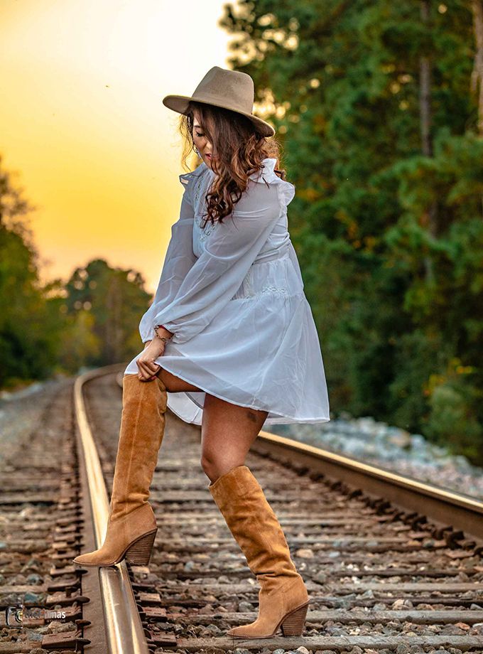 White dress and brown boots fashion shoot on railroad tracks at sunset.