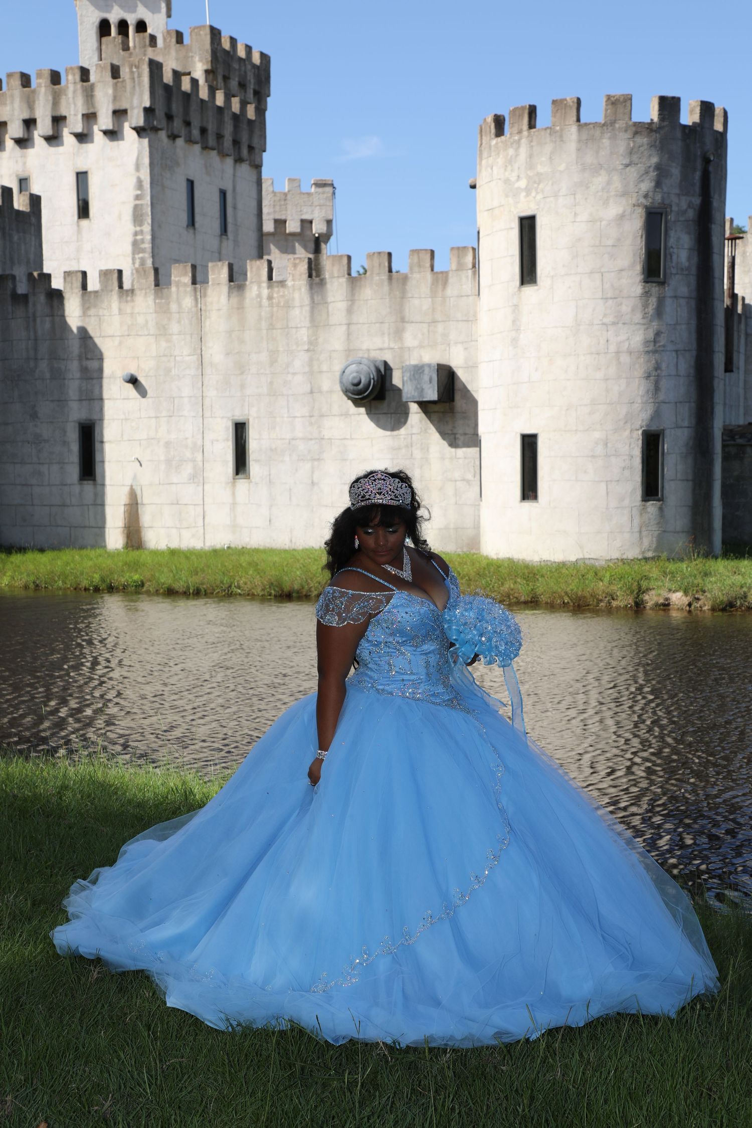 A person in a blue ball gown poses in front of a medieval-style castle with turrets.