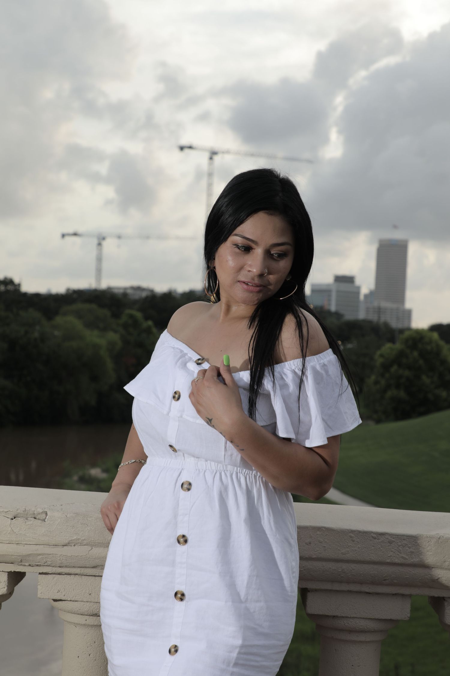 Urban fashion portrait in a white off-shoulder dress with city skyline and cranes in background.