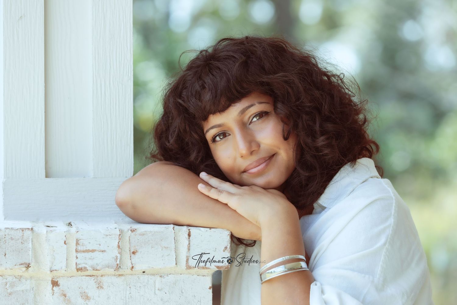 A person with dark curly hair rests their head on their hand while sitting near a window in natural light.