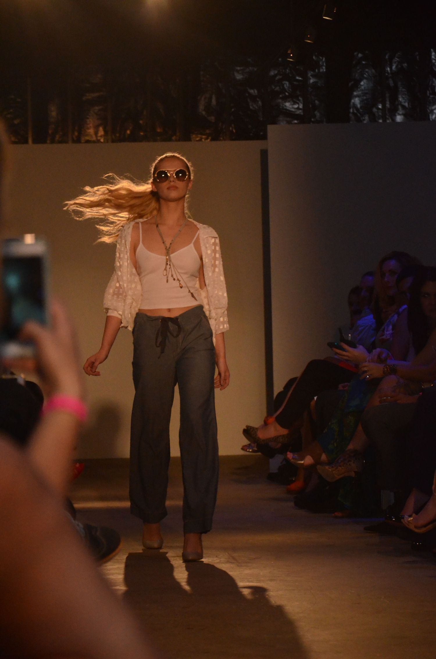 Model in casual attire walking runway with flowing hair and sunglasses.