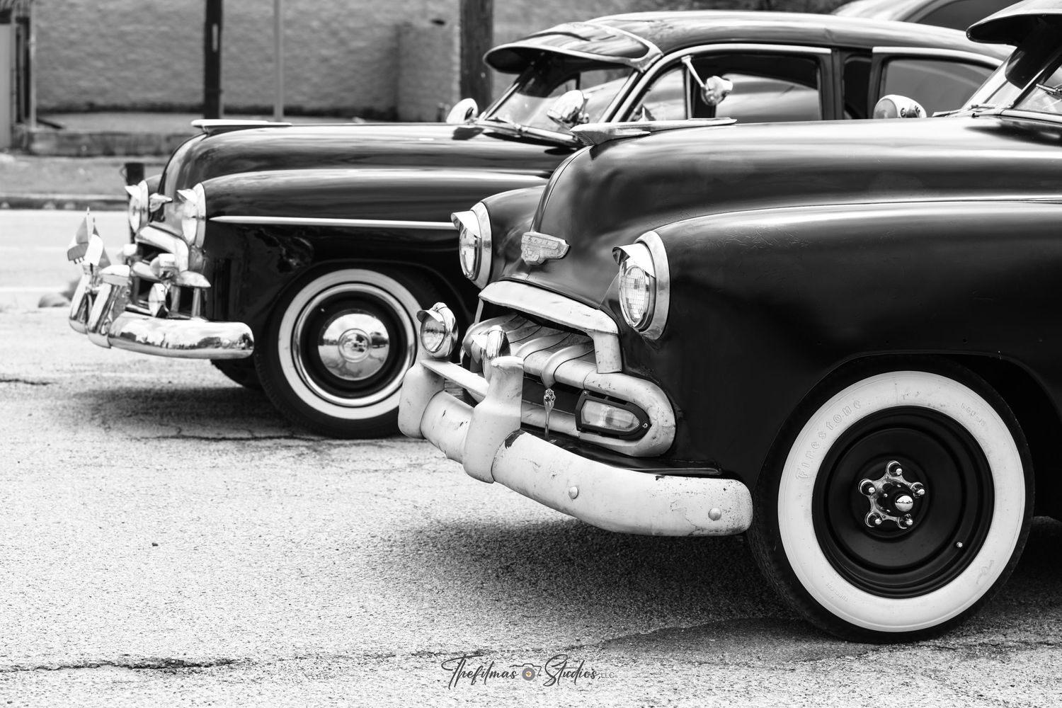 Black and white vintage cars with chrome trim and white wall tires line up in formation.