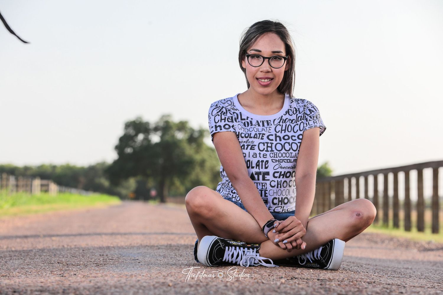 A casual portrait taken on a paved pathway with rustic fencing in the background.