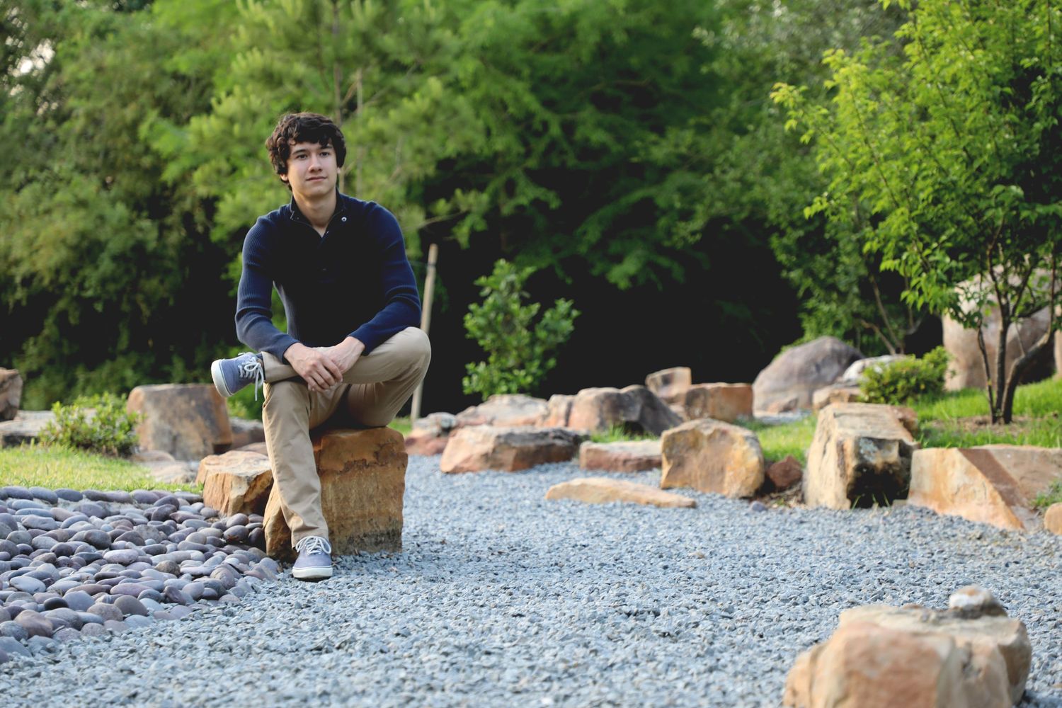 Person sits on rock with scenic garden and decorative stones in background.