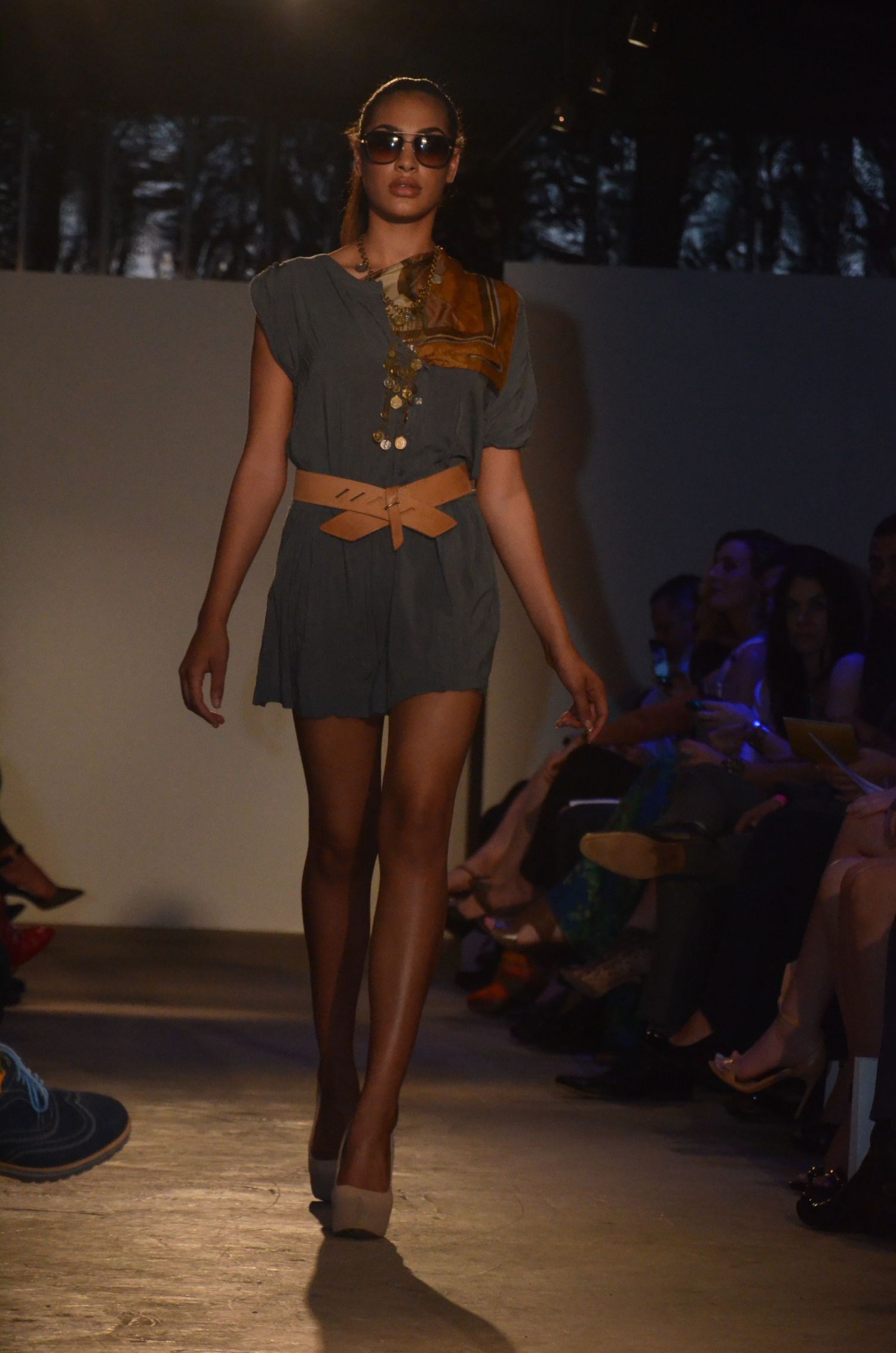 Model walks runway in grey two-piece outfit with cutout detail during fashion show.