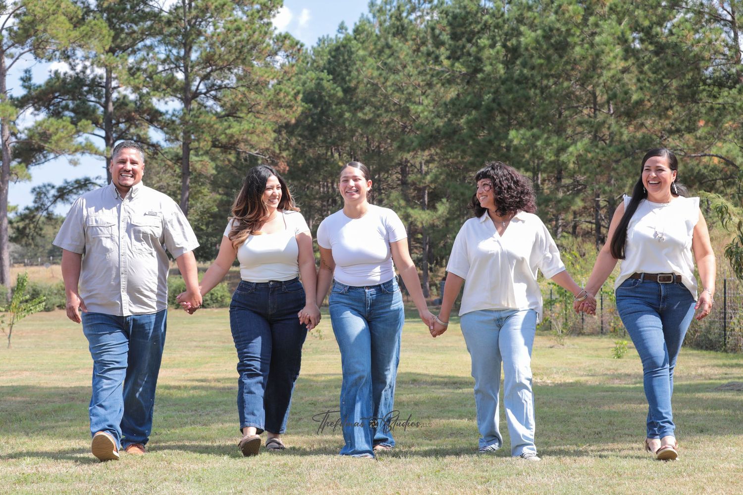 A sequence of people walking in jeans and white shirts on grass with trees in the background.