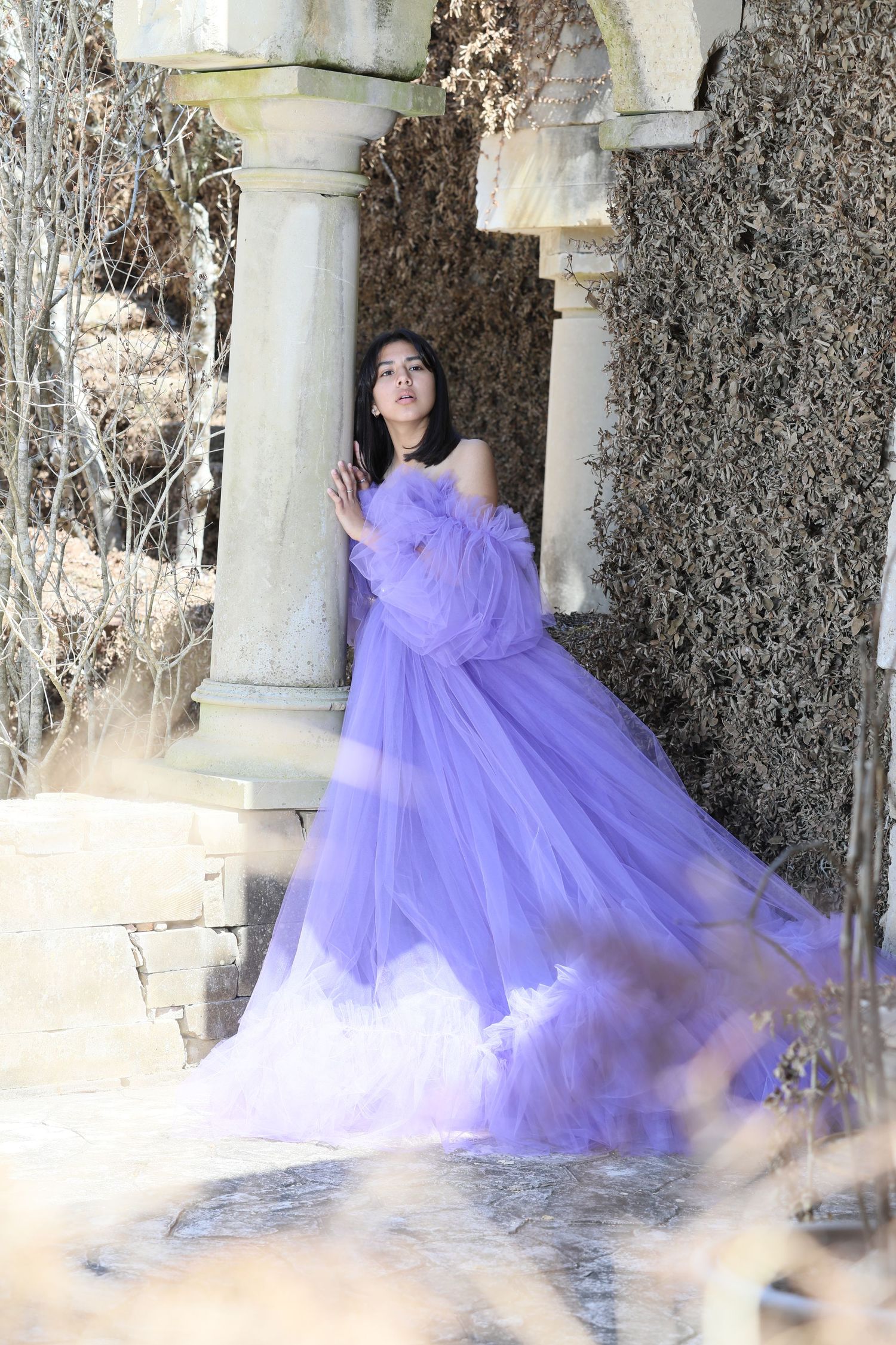Ethereal purple tulle gown photographed among stone columns and winter foliage.