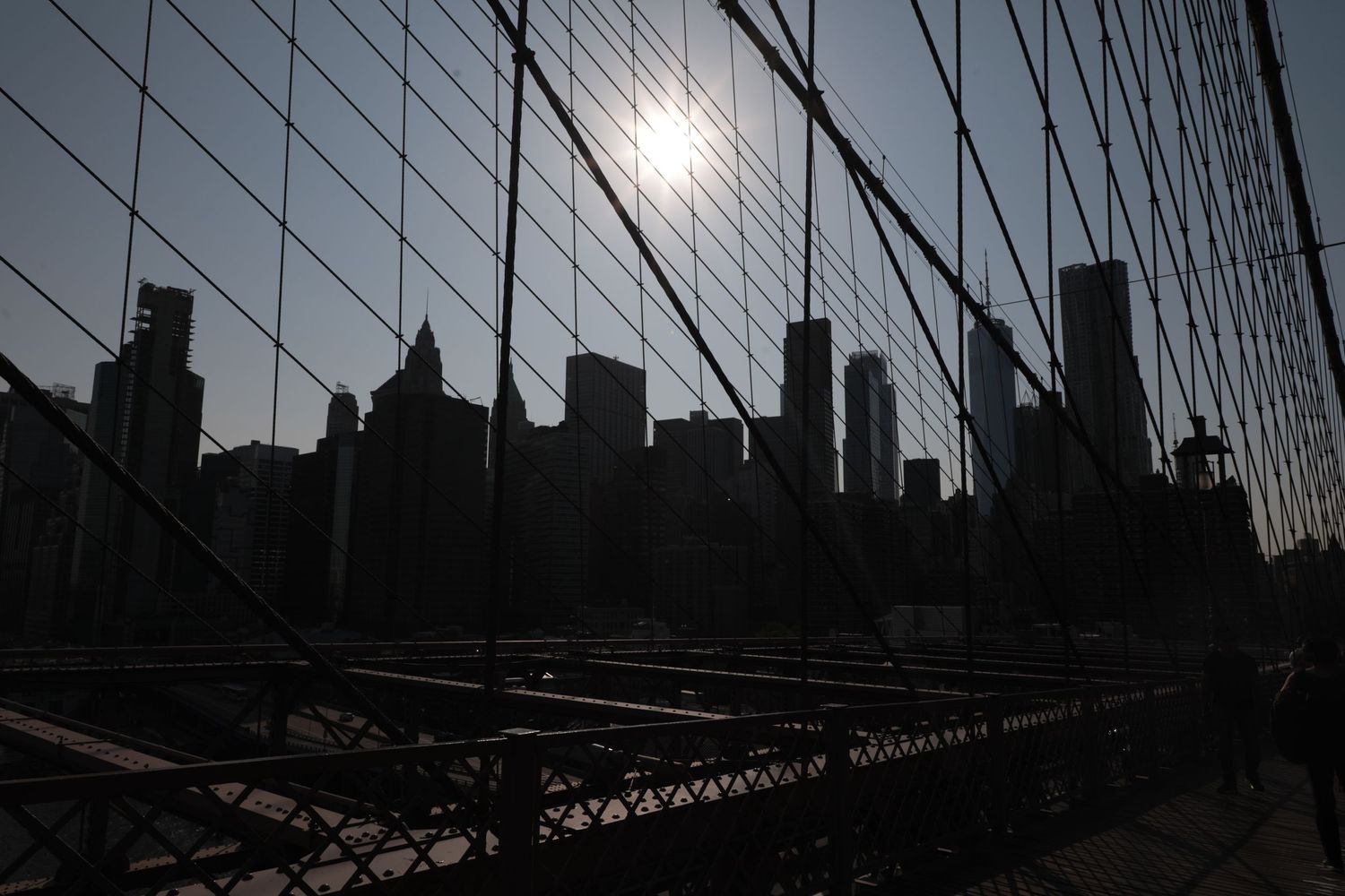 Silhouette of New York City skyline viewed through Brooklyn Bridge cables at sunset.
