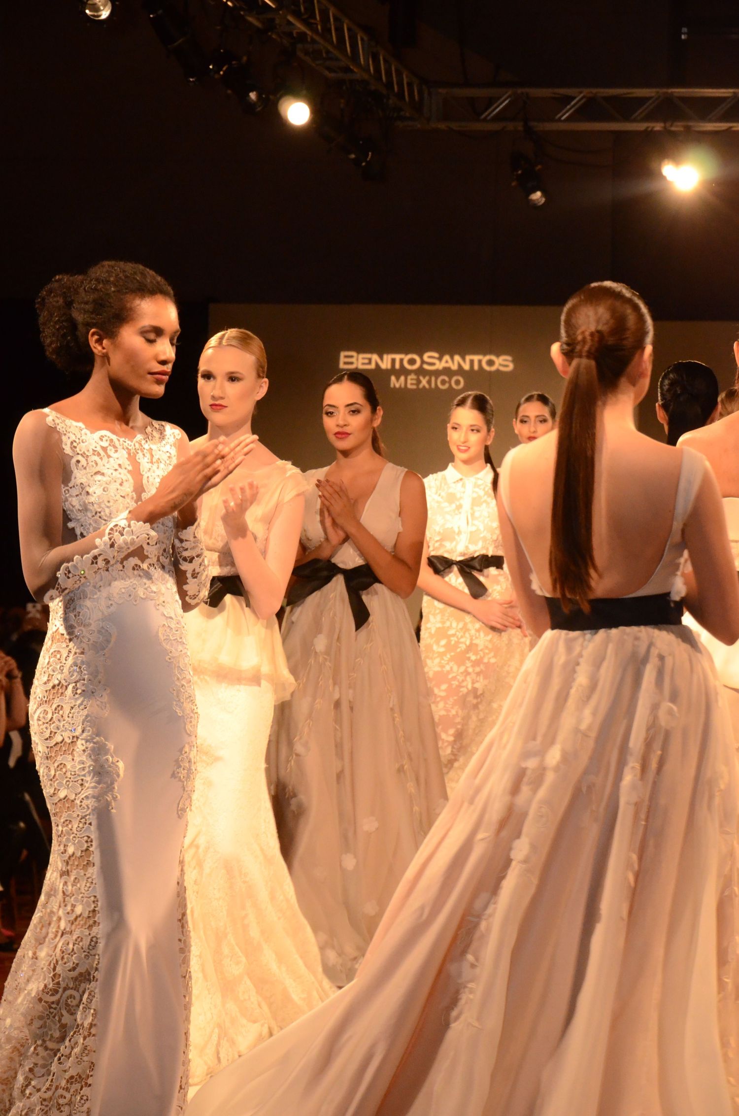 Models showcase elegant white wedding gowns on a fashion runway.