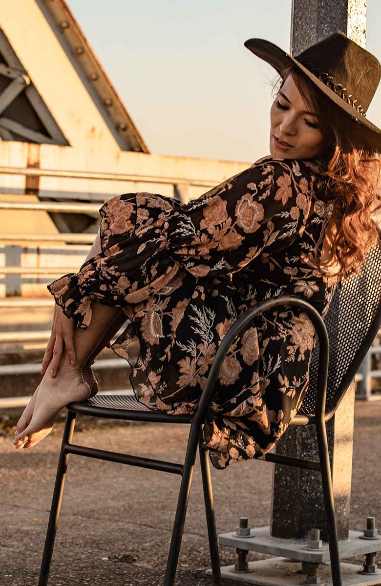 Artistic sunset portrait of person in floral dress and hat relaxing in metal chair.