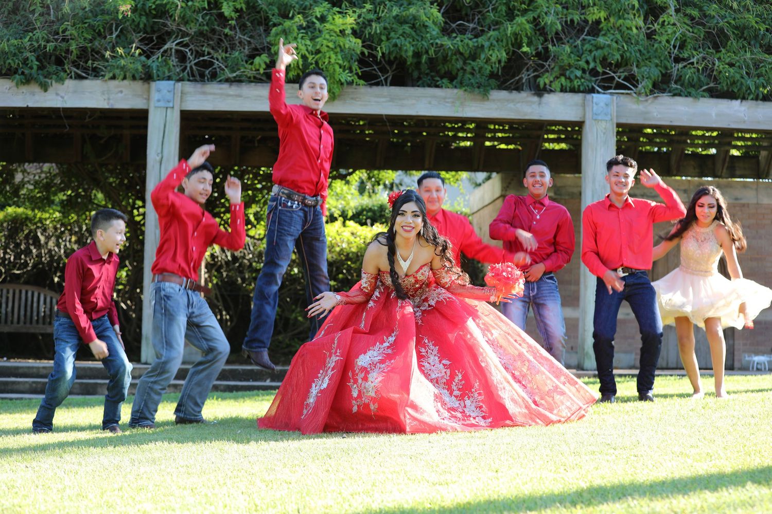A celebration scene with people in red shirts surrounding someone in a red ball gown on grass.