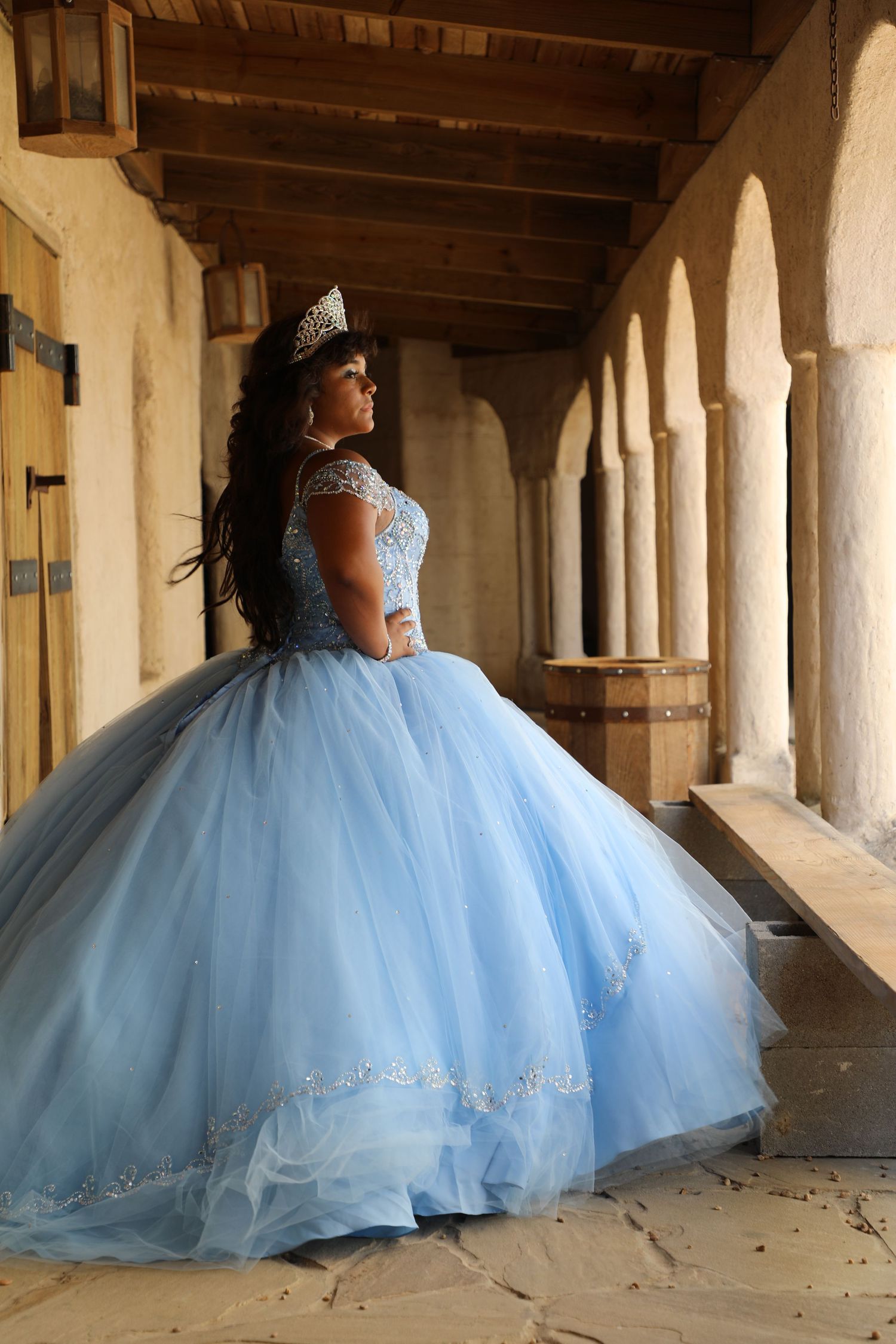 A flowing light blue ballgown with crystal details photographed in an elegant archway corridor.