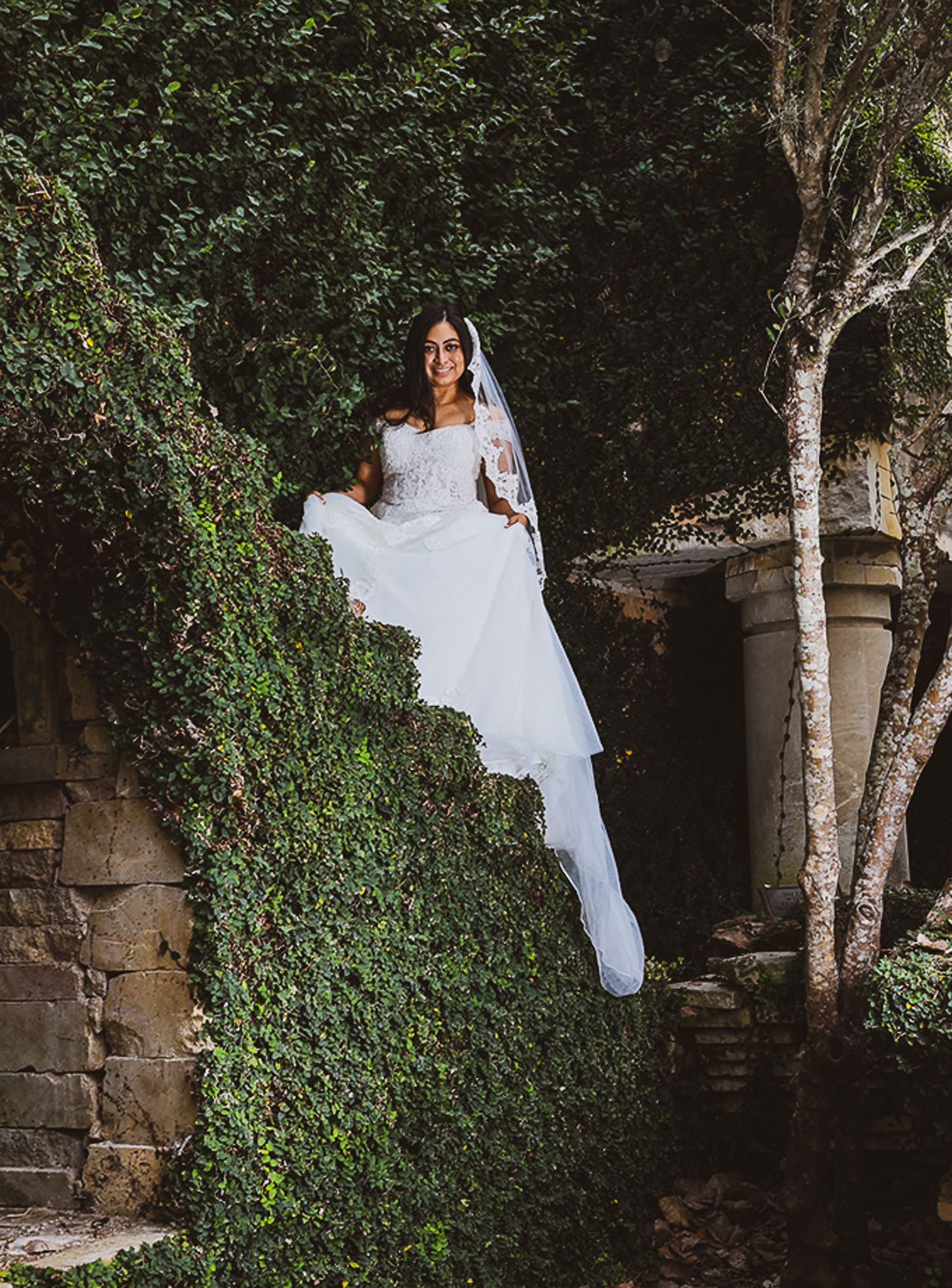 Dramatic bridal portrait on ivy-covered wall in enchanted garden setting.